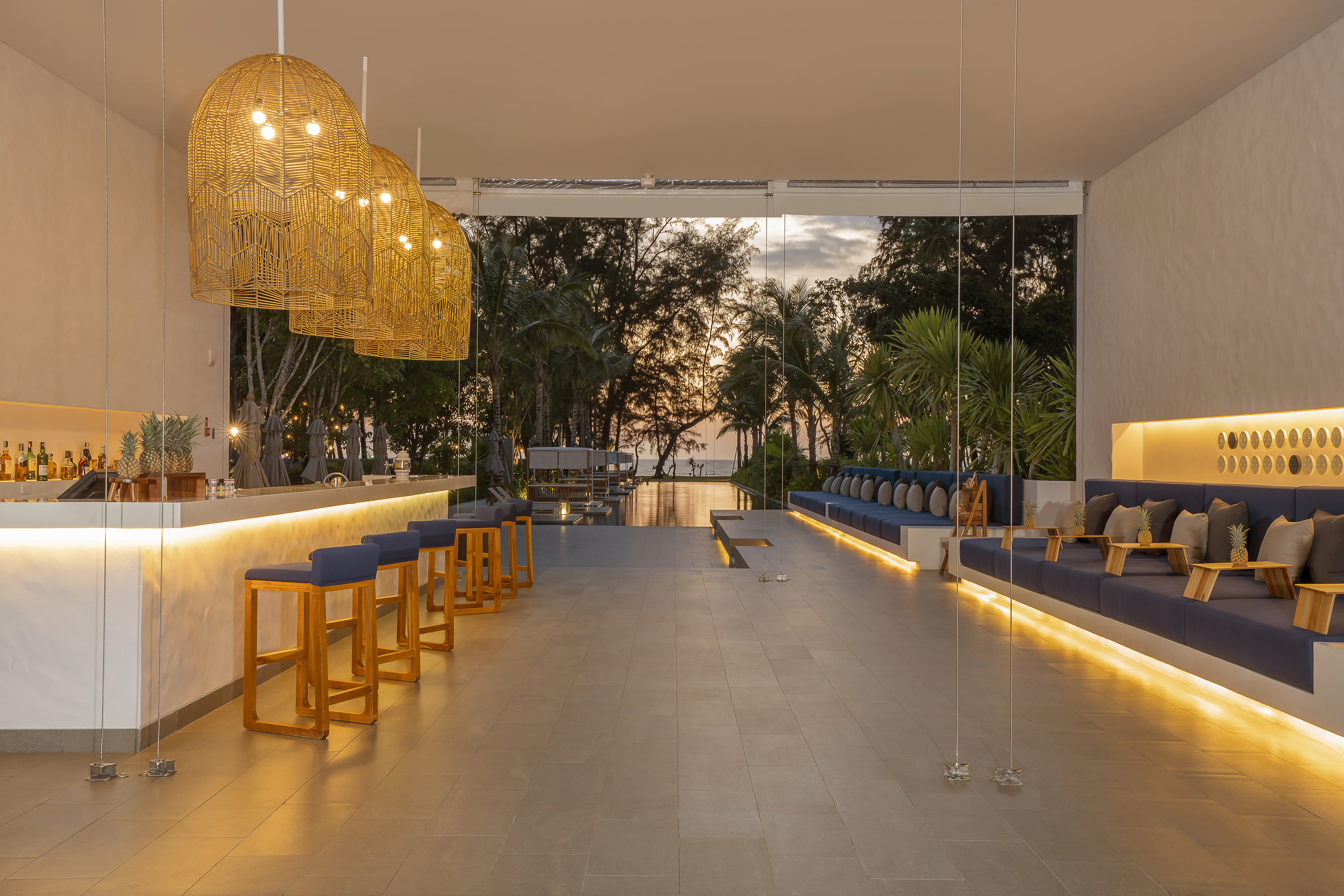 Elegant resort bar lounge with woven pendant lights and ocean sunset view.