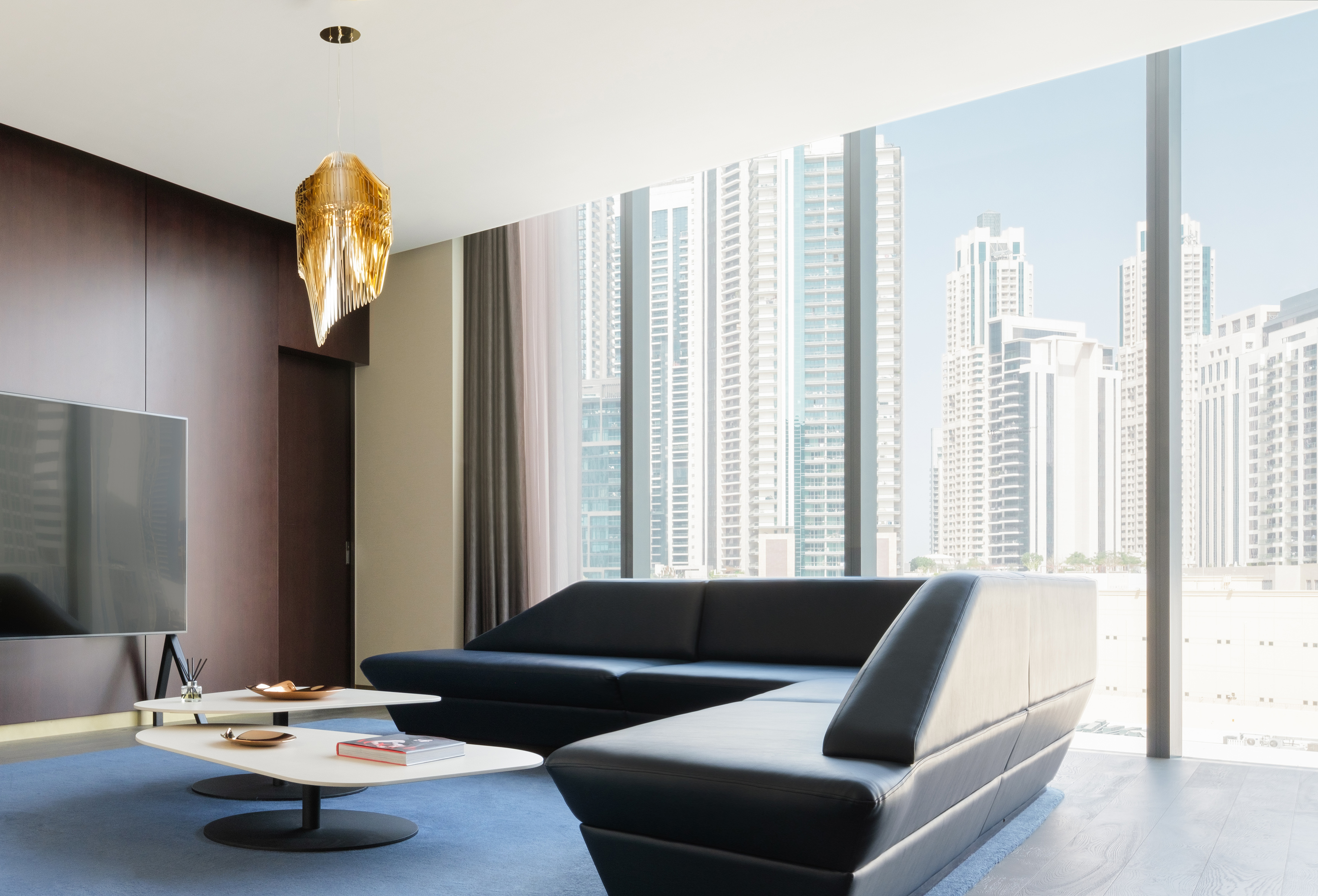Modern luxury living room, black sofa, city view, gold chandelier, blue rug.