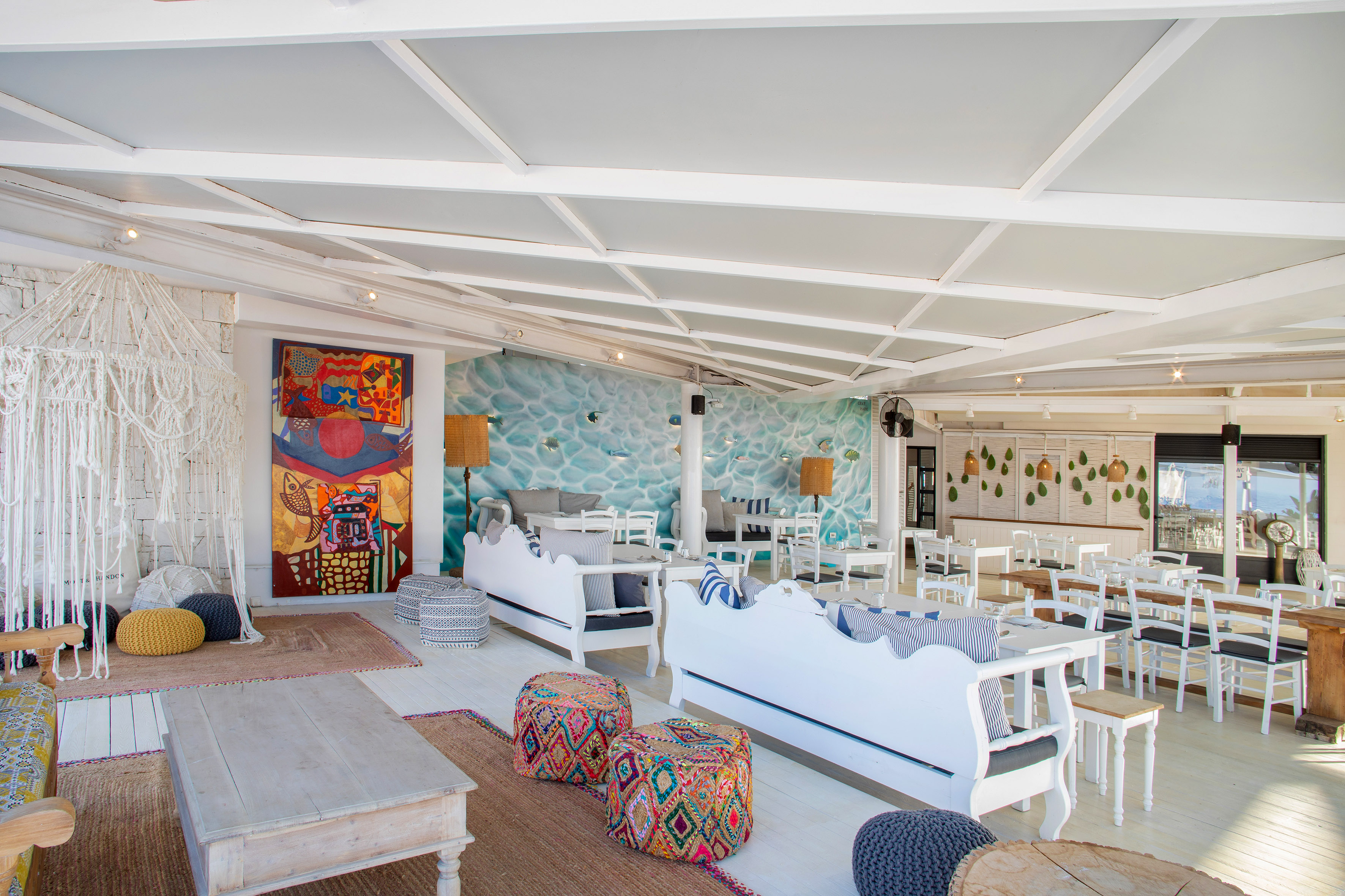 Spacious, bright beach lounge interior with white furniture, vibrant art, and ocean mural.