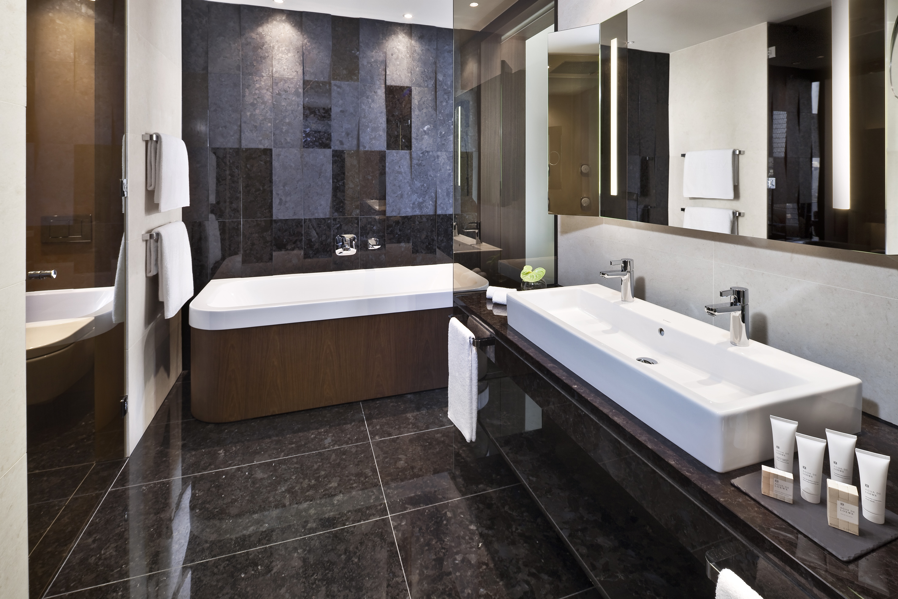 Luxury bathroom with dark granite tiles, modern bathtub, and double vanity.