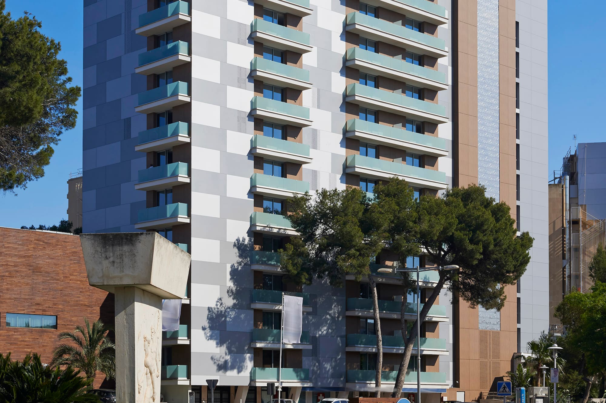Modern high-rise building with balconies, patterned facade, and urban roundabout.