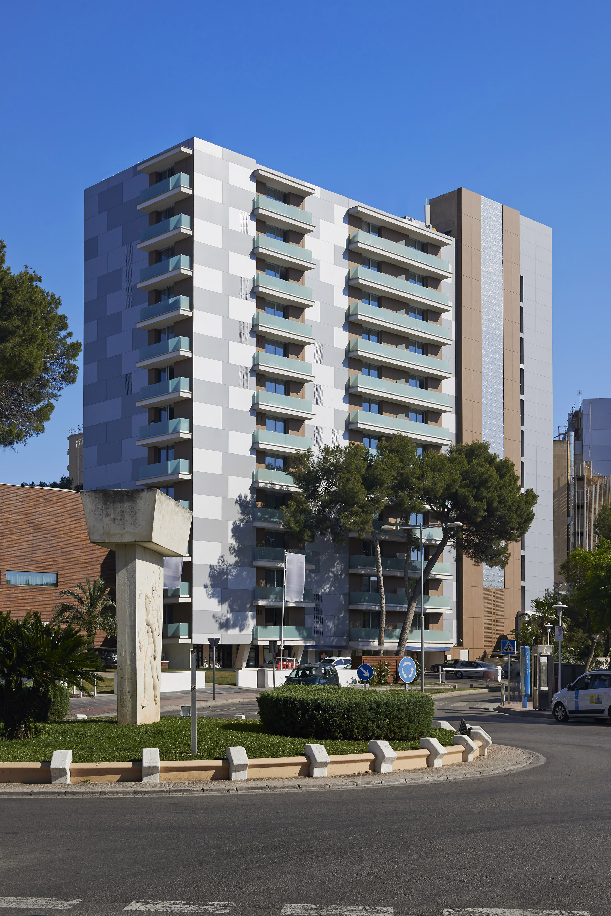 Modern high-rise building with balconies, patterned facade, and urban roundabout.