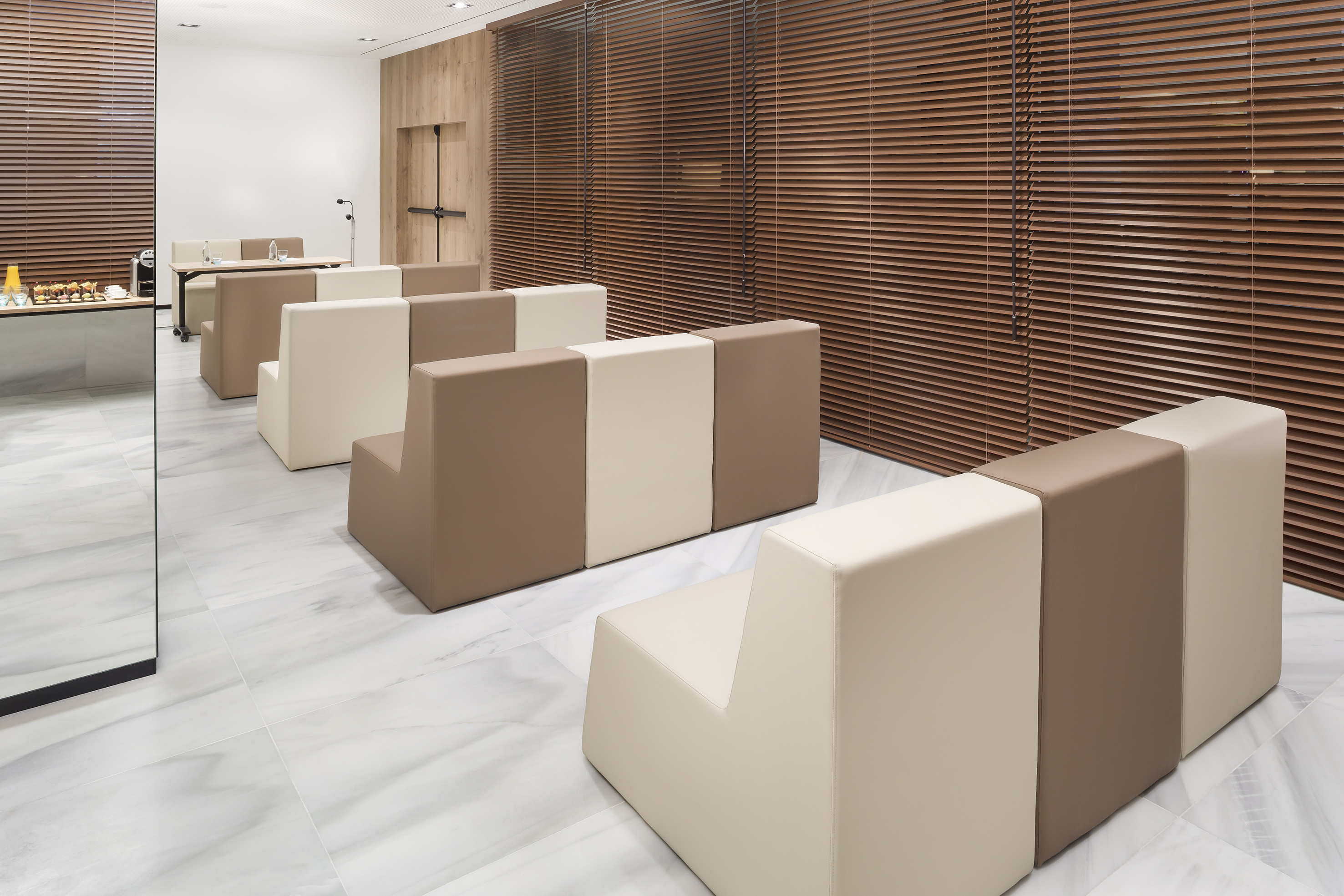 Contemporary waiting area with modular beige/brown sofas, marble, and wood blinds.