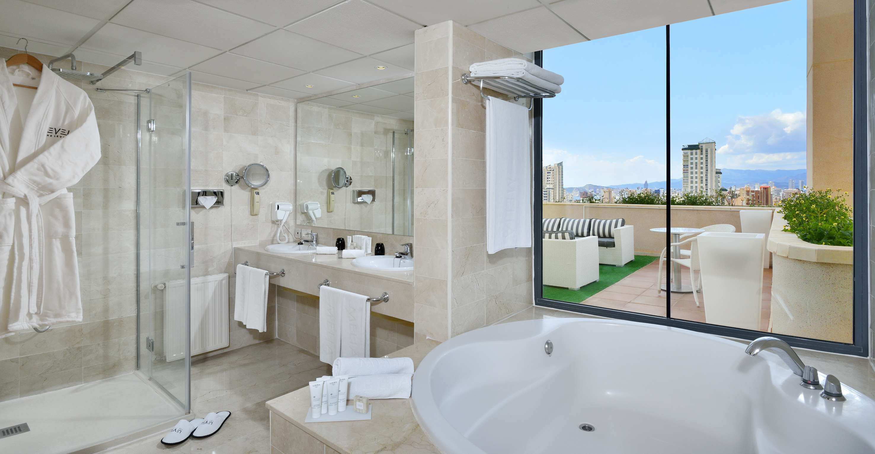 Modern hotel bathroom with tub, shower, vanity, and private city view terrace.