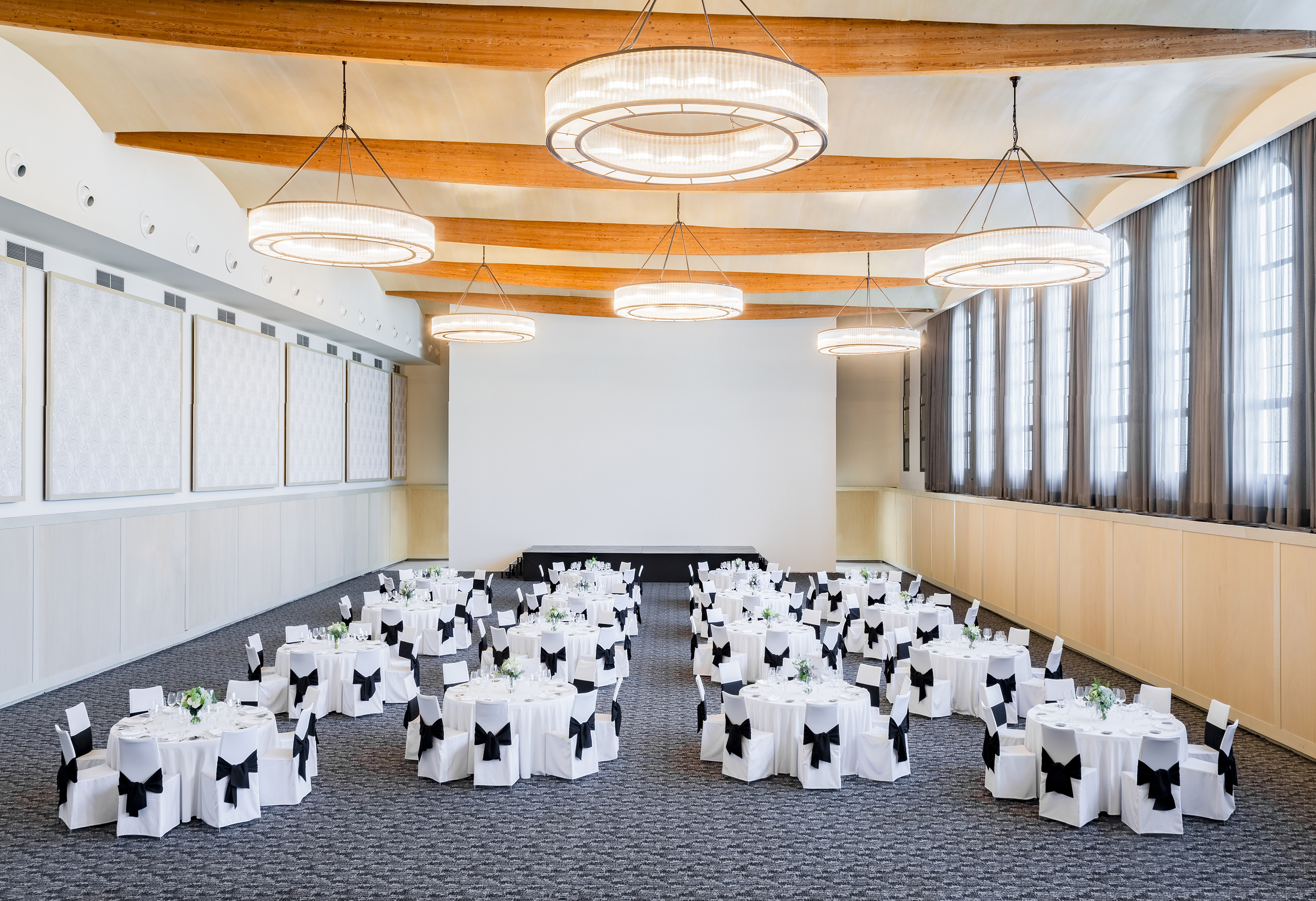 Elegant ballroom with banquet tables, black bow chairs, and modern chandeliers.