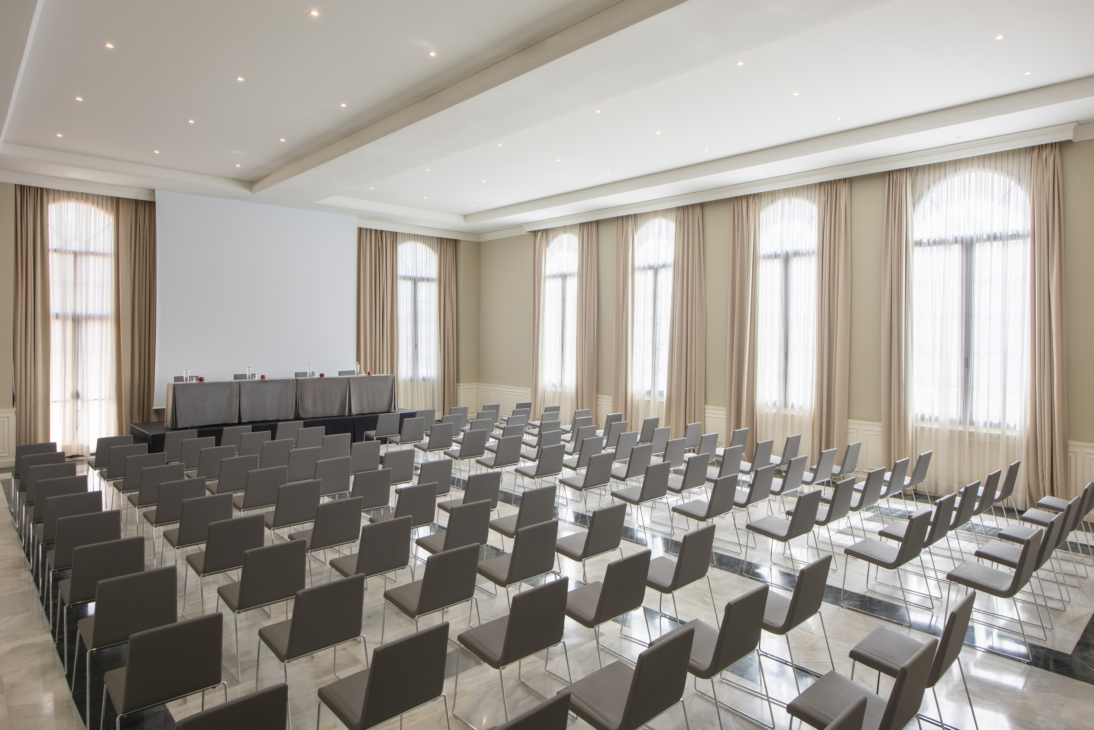 Spacious conference room with theater seating, presentation screen, and bright windows.