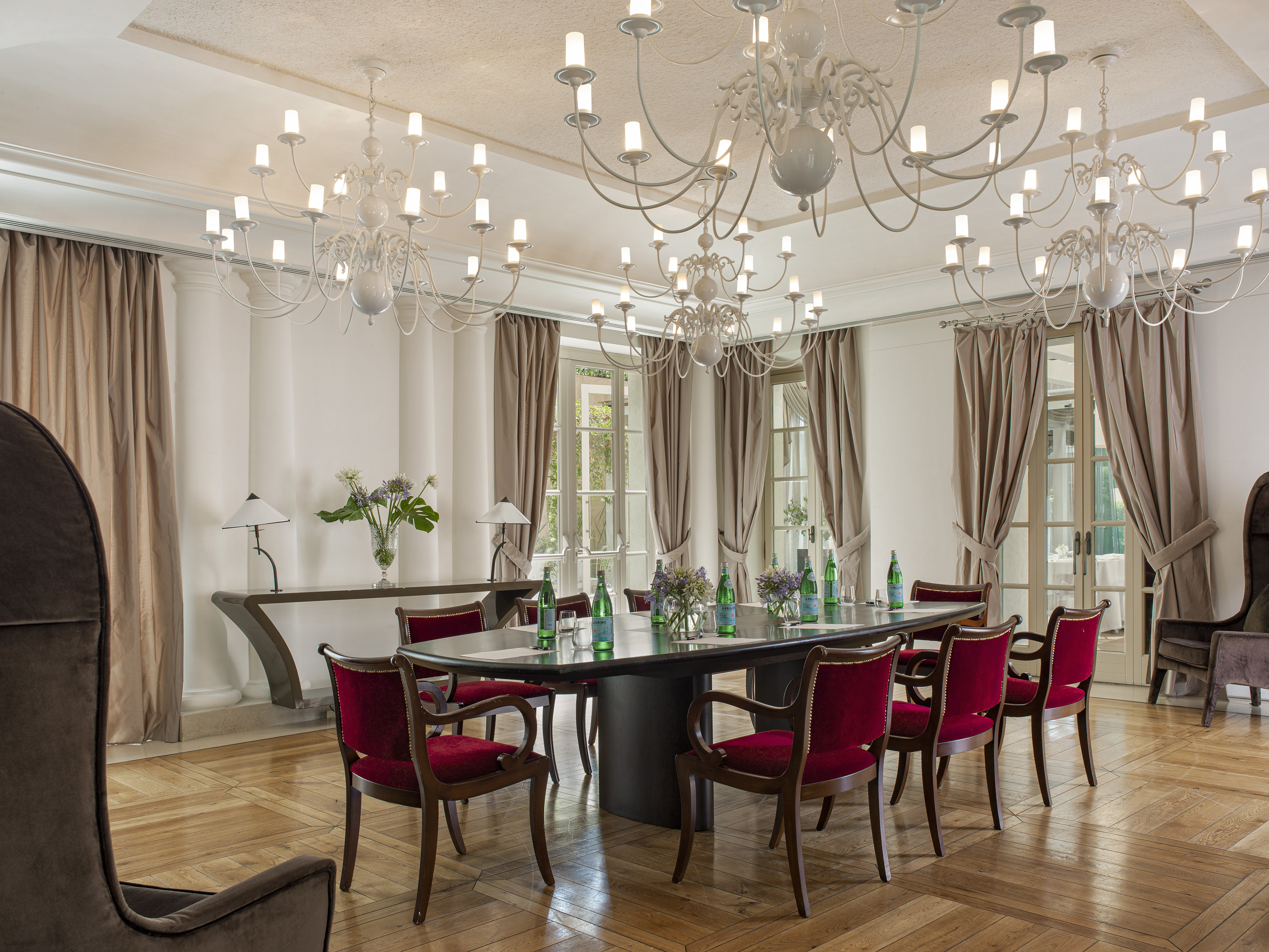 Grand conference room with long table, red velvet chairs, and white chandeliers.