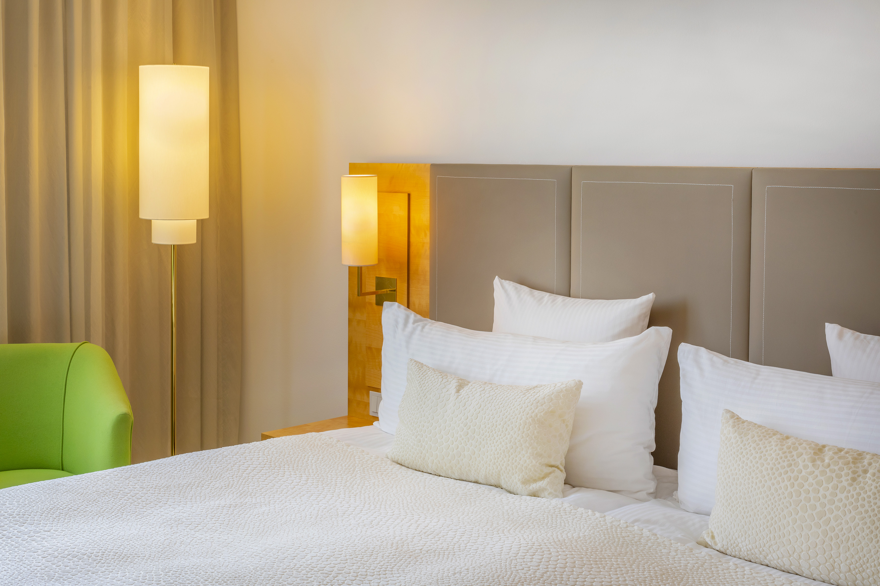 Hotel bedroom interior with white bed, beige headboard, and warm lighting.