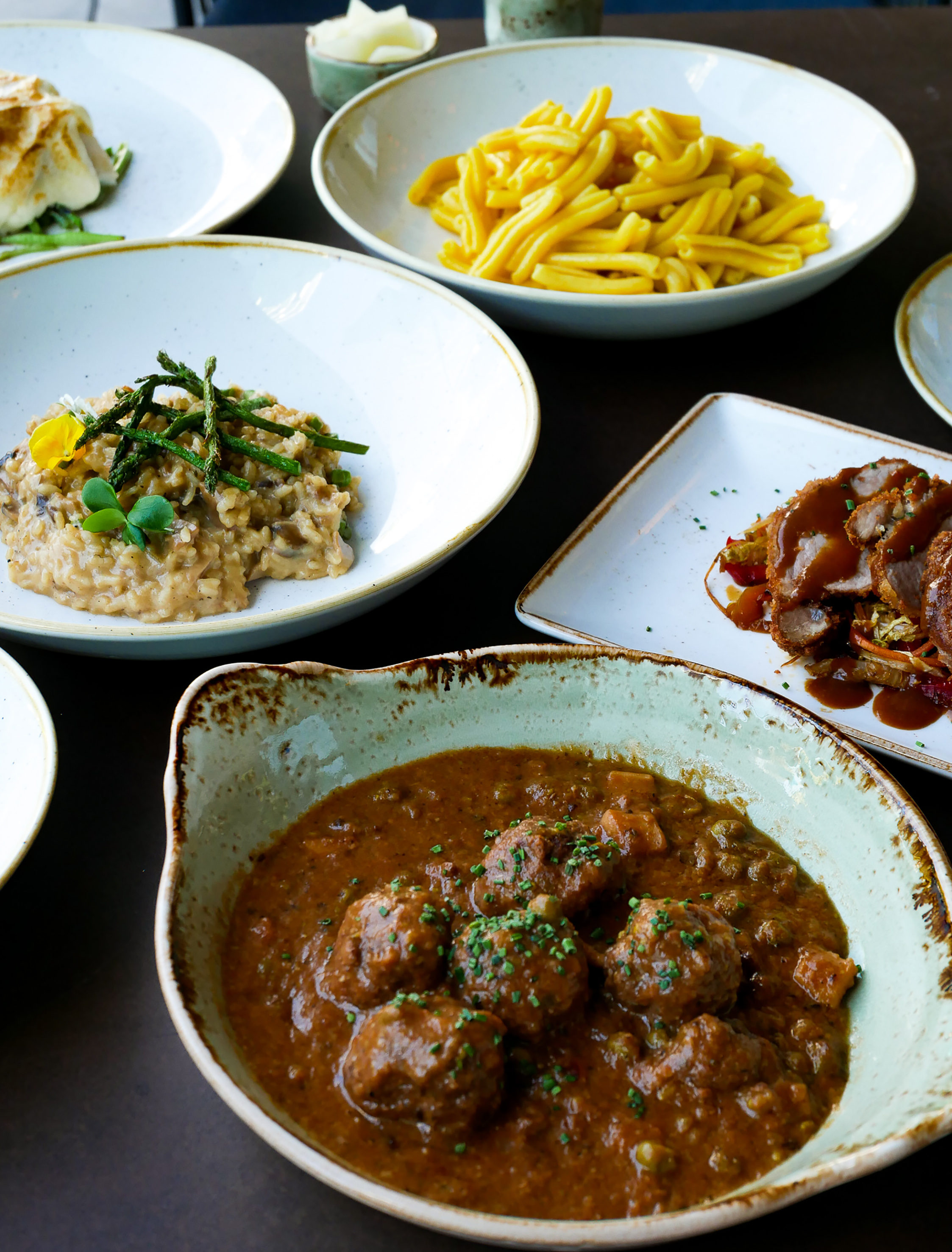 Restaurant meal with meatballs, mushroom risotto, pasta, and sliced meat.