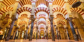 a large room with columns and arches with Mosque–Cathedral of Córdoba in the background