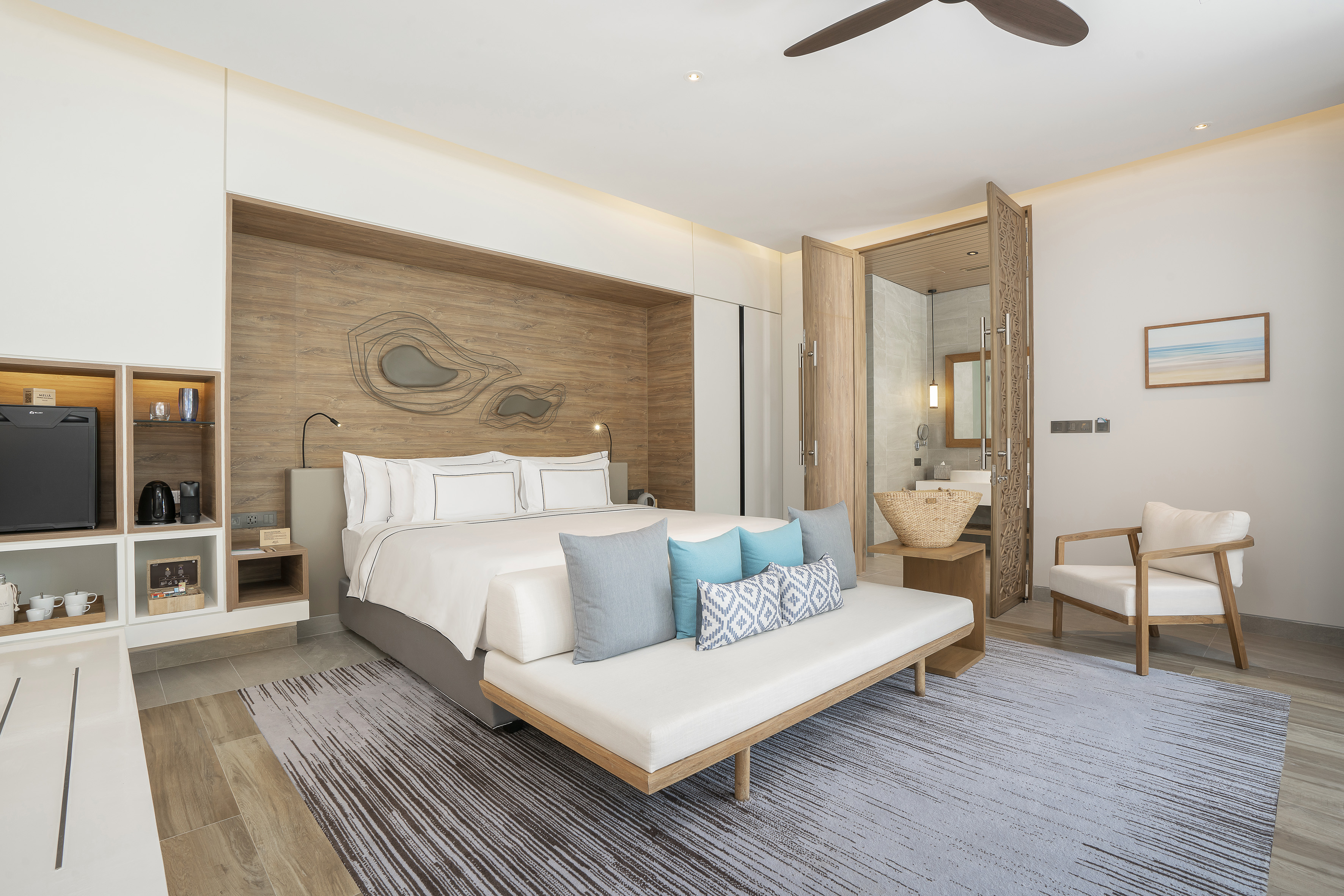 Modern hotel bedroom with king bed, wooden headboard, blue pillows, and open bath.