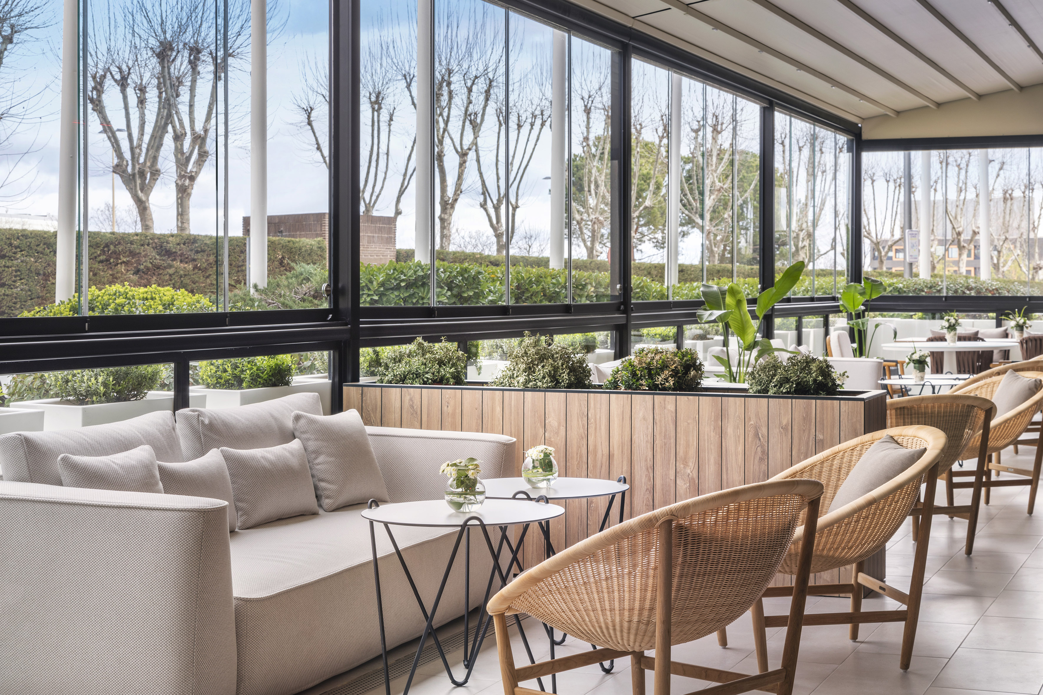 Bright hotel lounge with modern sofa, wicker chairs, and panoramic windows.