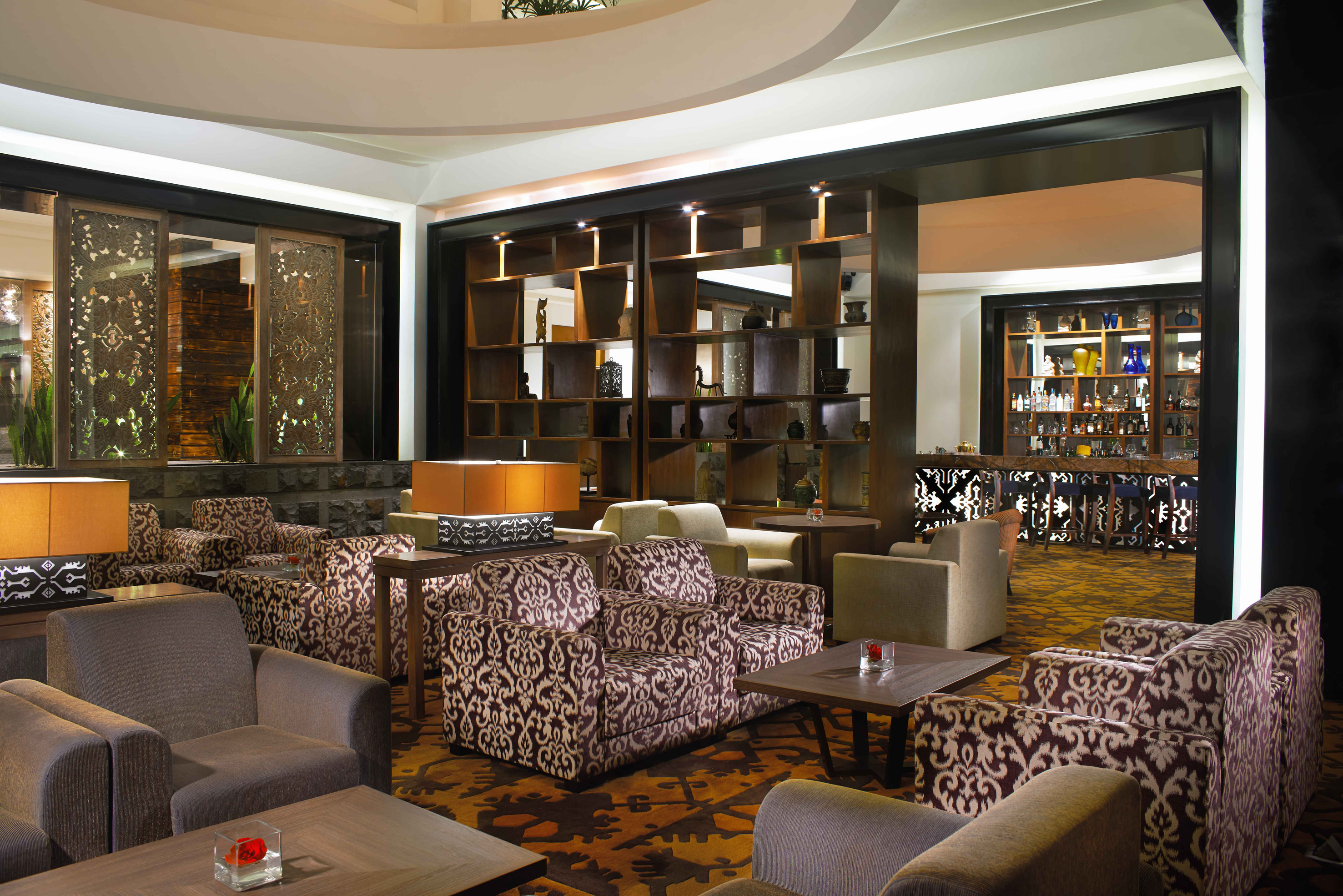 Elegant hotel lounge with patterned armchairs, decorative shelving, and a bar area.