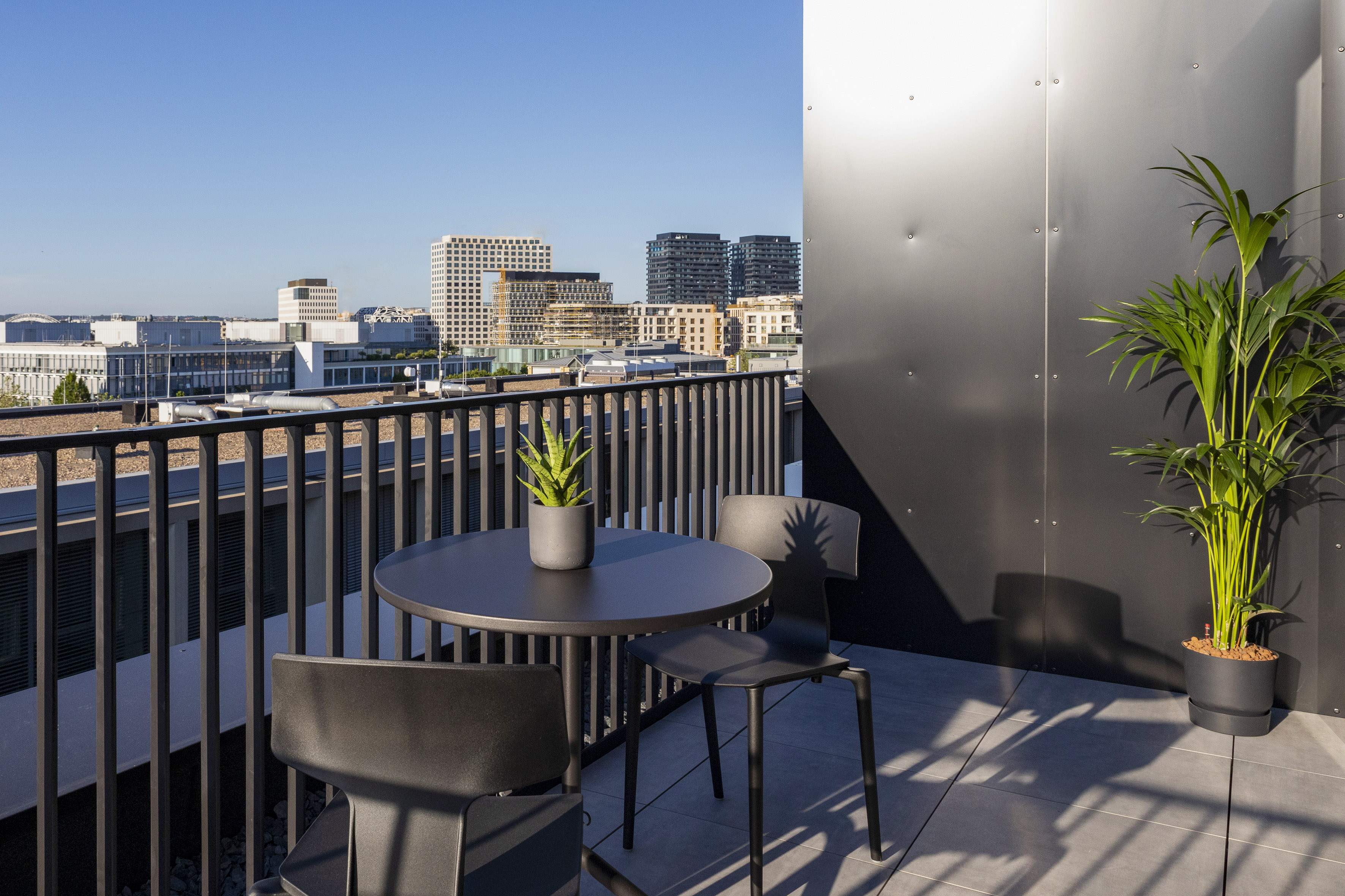 Modern rooftop terrace with outdoor table, chairs, plants, and city view.