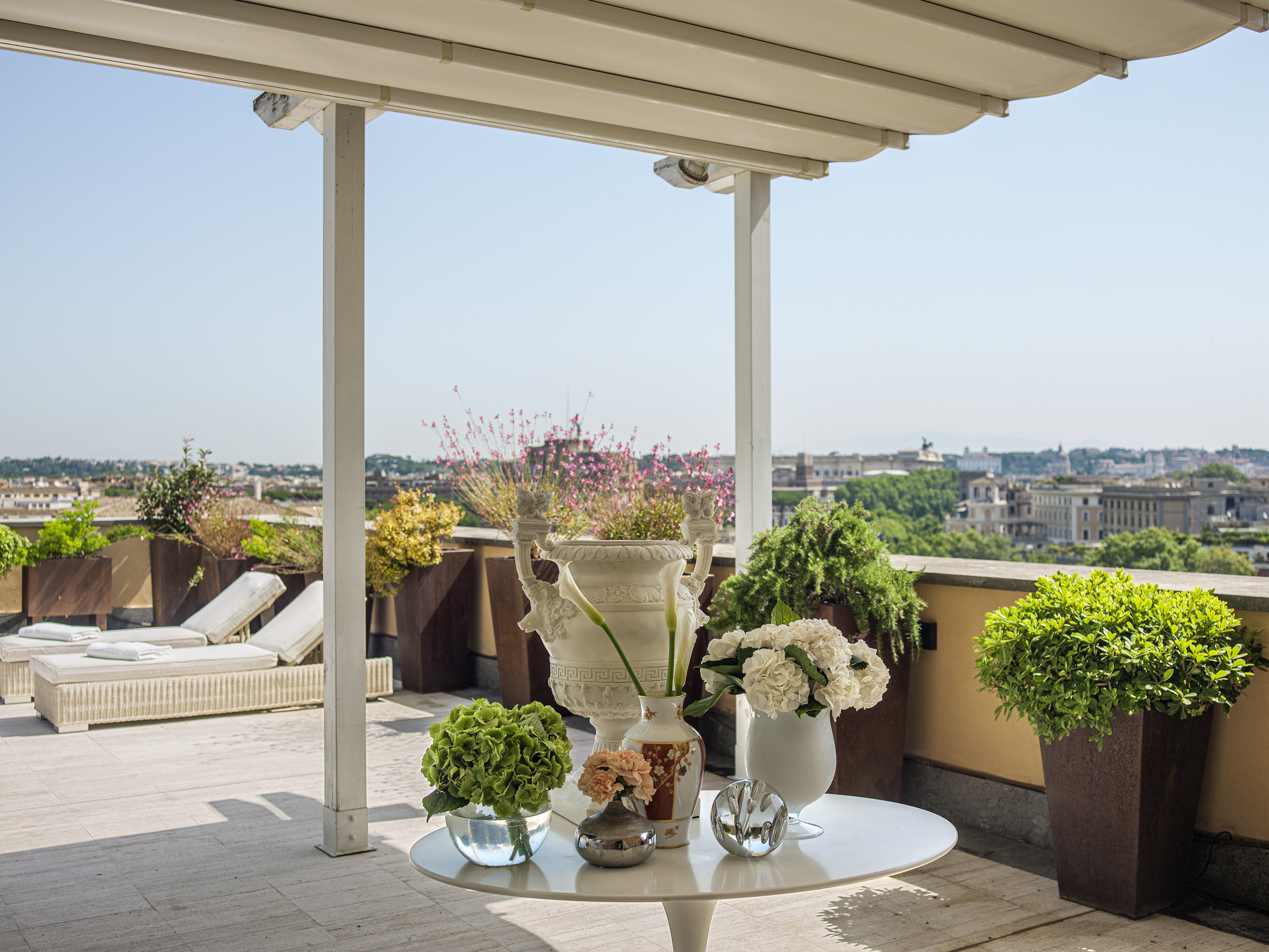 Rooftop terrace with flower arrangements, lounge seating, and city view.