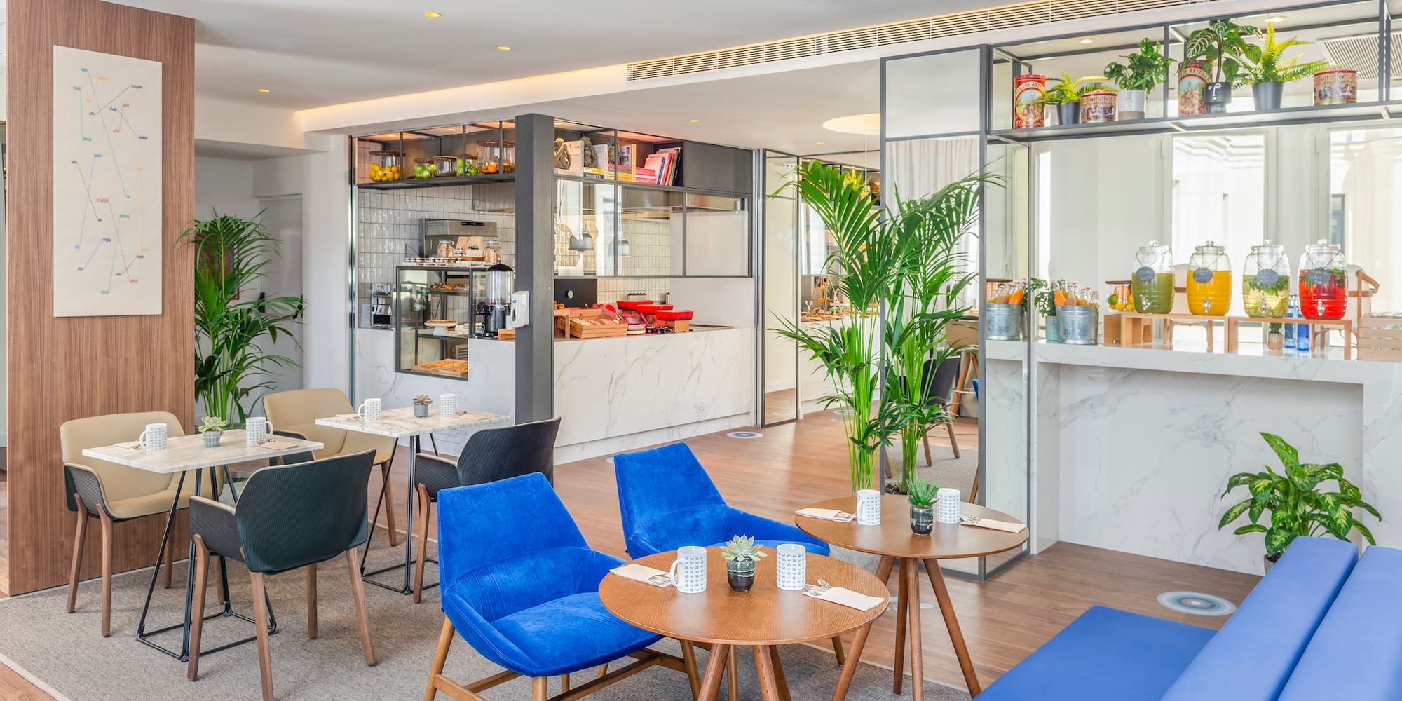 Modern hotel cafe interior with blue chairs, coffee bar, and juice dispensers.