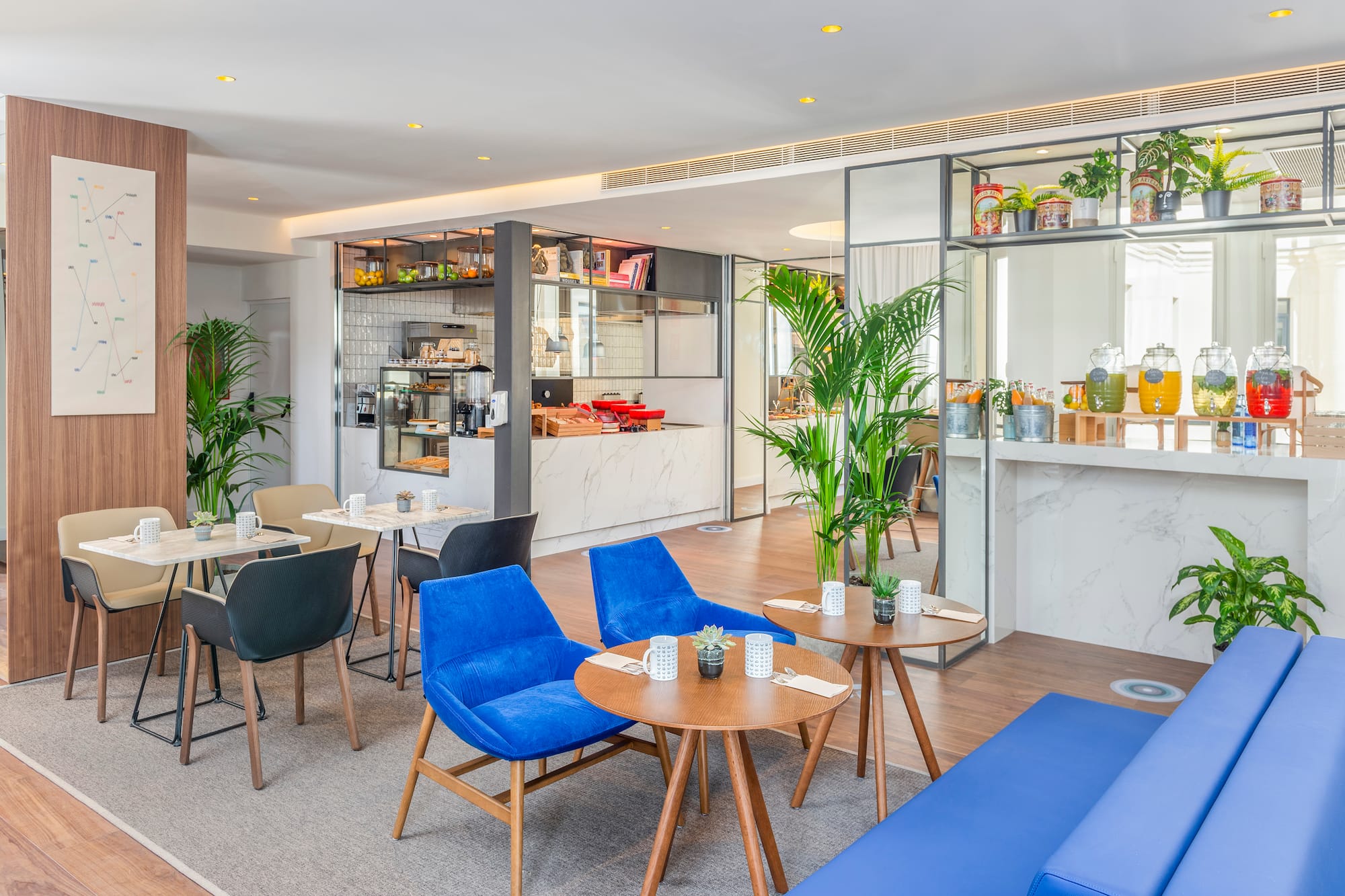 Modern hotel cafe interior with blue chairs, coffee bar, and juice dispensers.