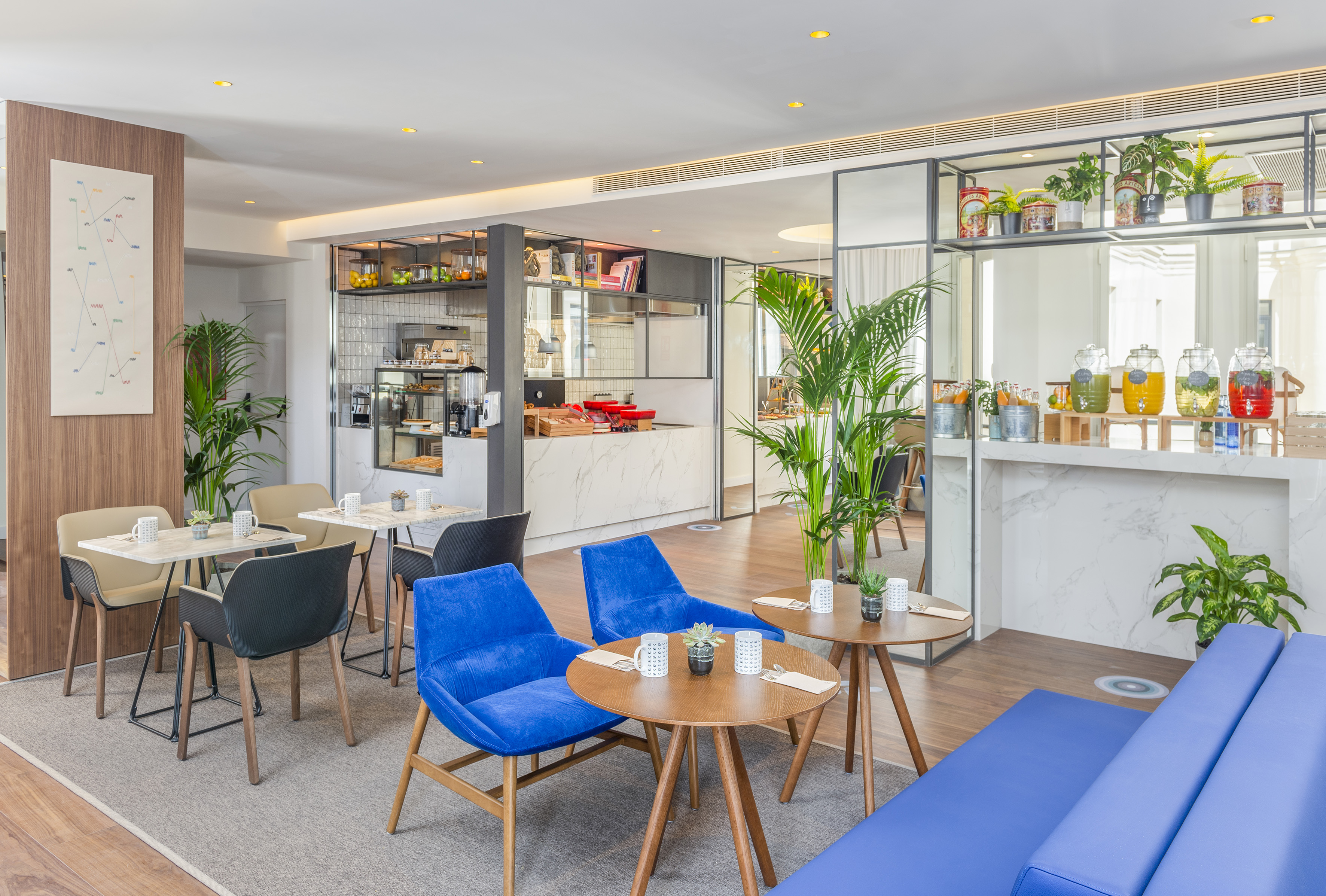 Modern hotel cafe interior with blue chairs, coffee bar, and juice dispensers.