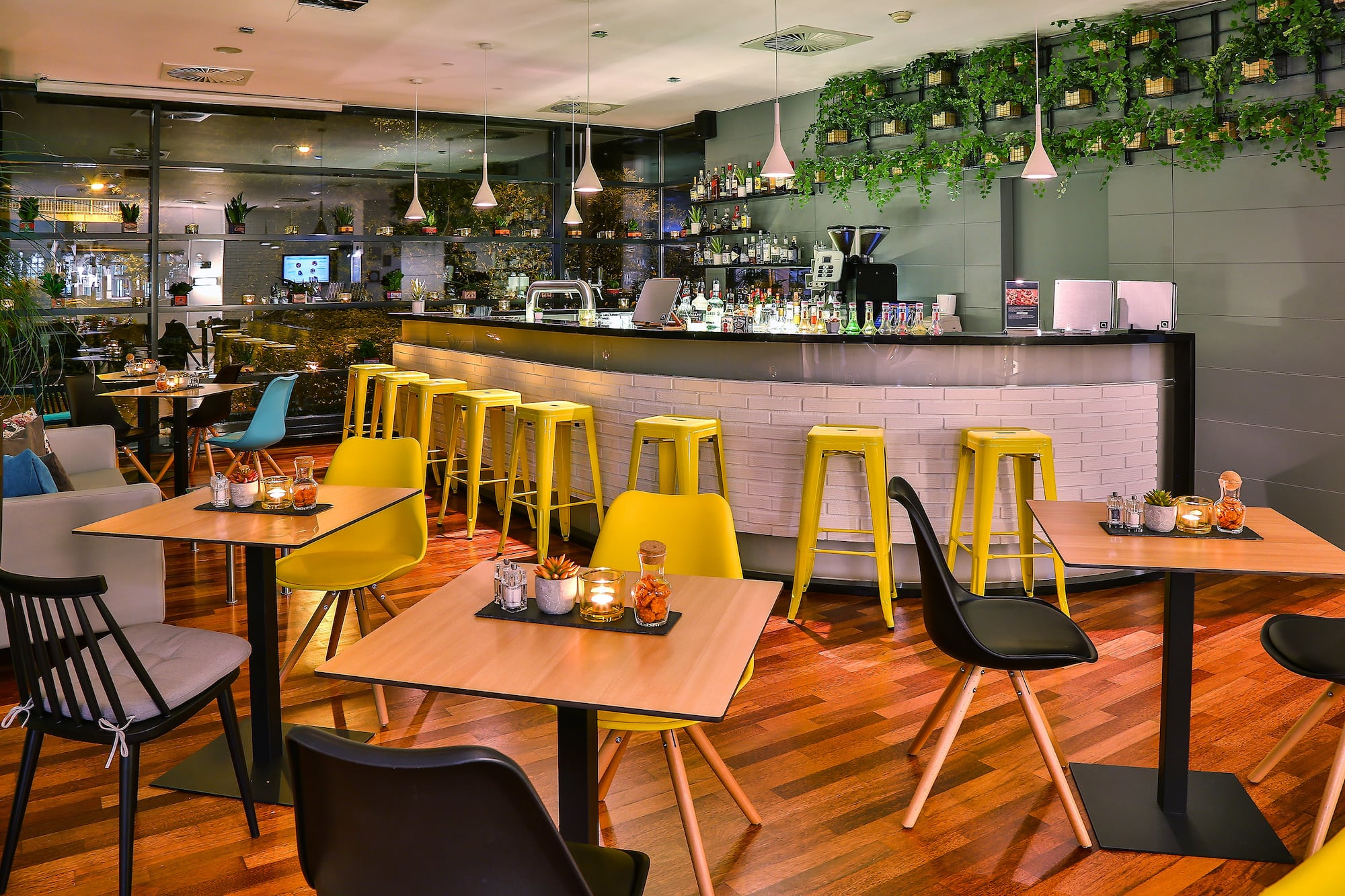 Modern cafe bar interior with yellow stools, warm lighting, and green wall decor.