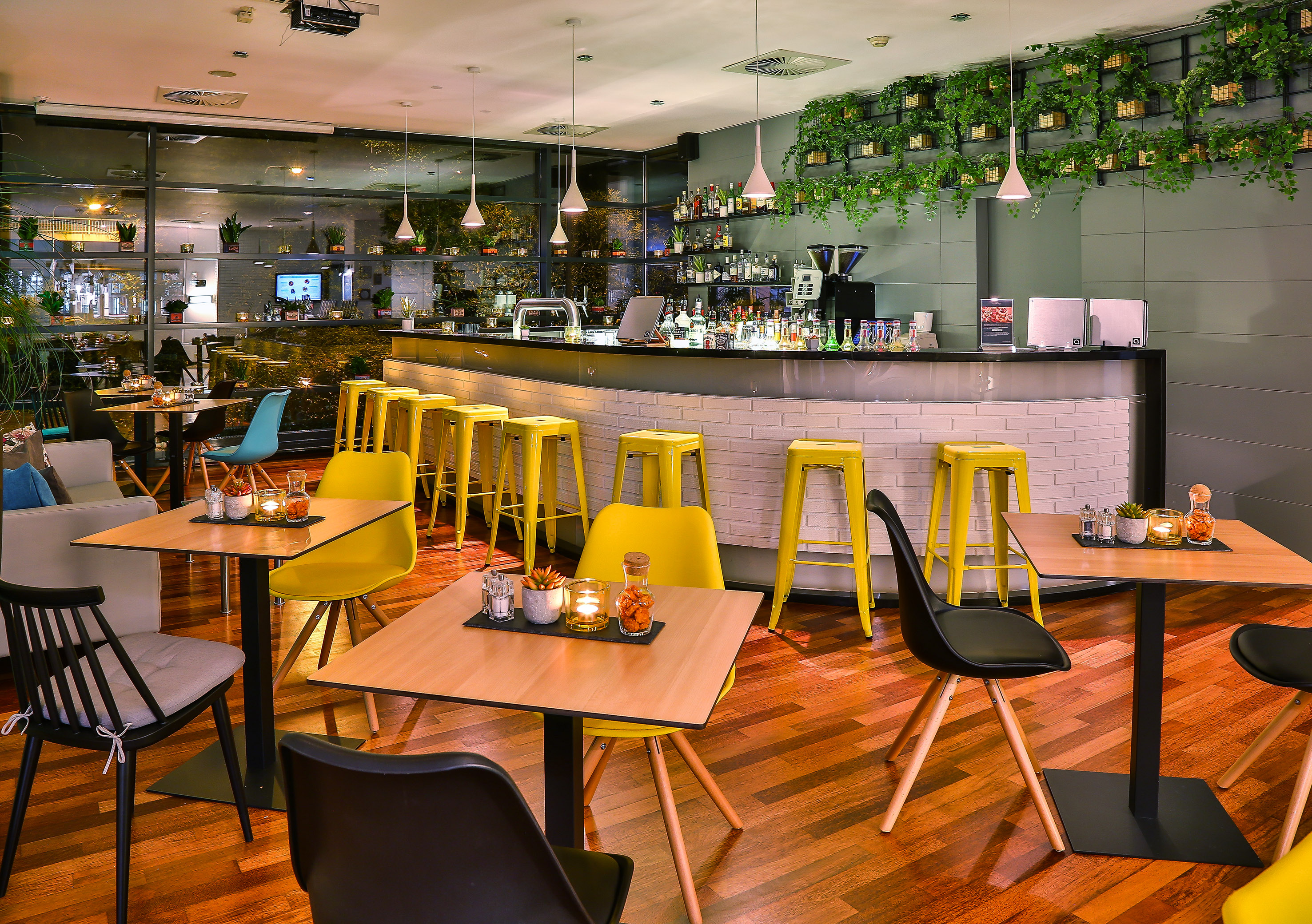 Modern cafe bar interior with yellow stools, warm lighting, and green wall decor.