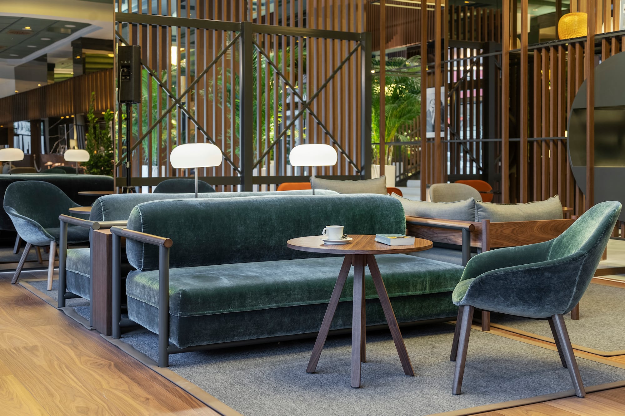 Modern hotel lounge with emerald velvet sofa, armchair, and wooden coffee table.