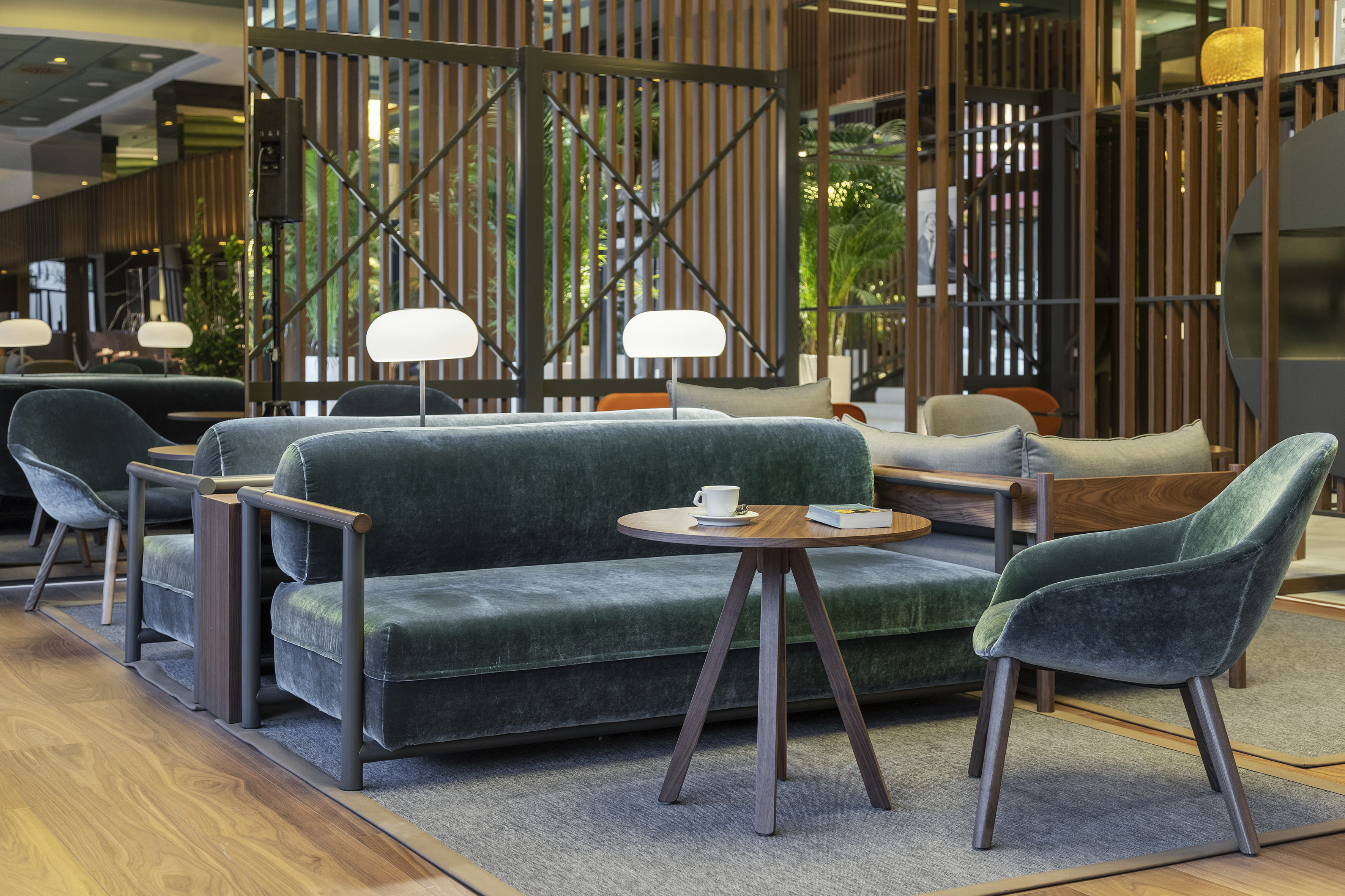 Modern hotel lounge with emerald velvet sofa, armchair, and wooden coffee table.