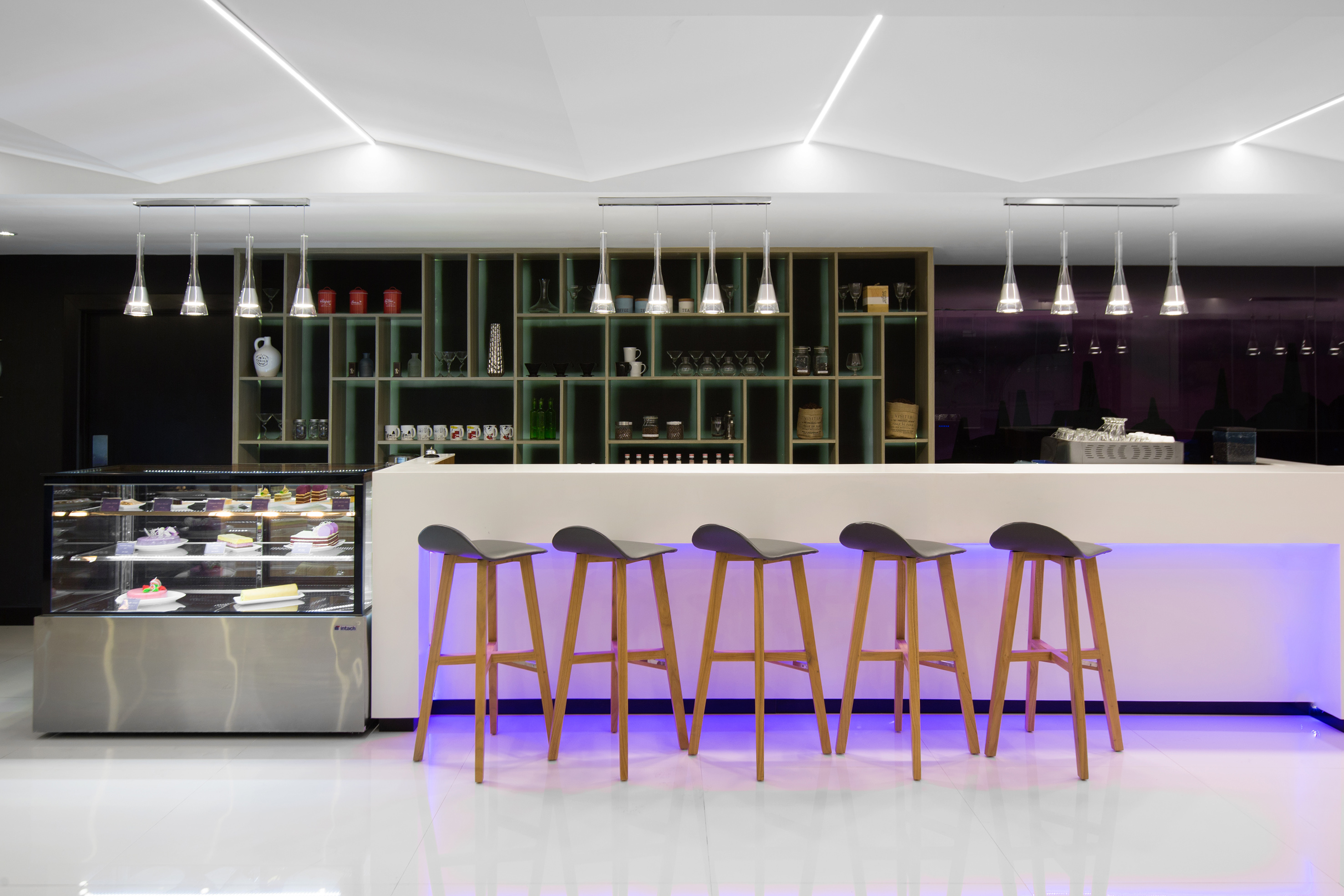 Cafe bar counter with purple LED lighting, five stools, dessert display, and shelves.