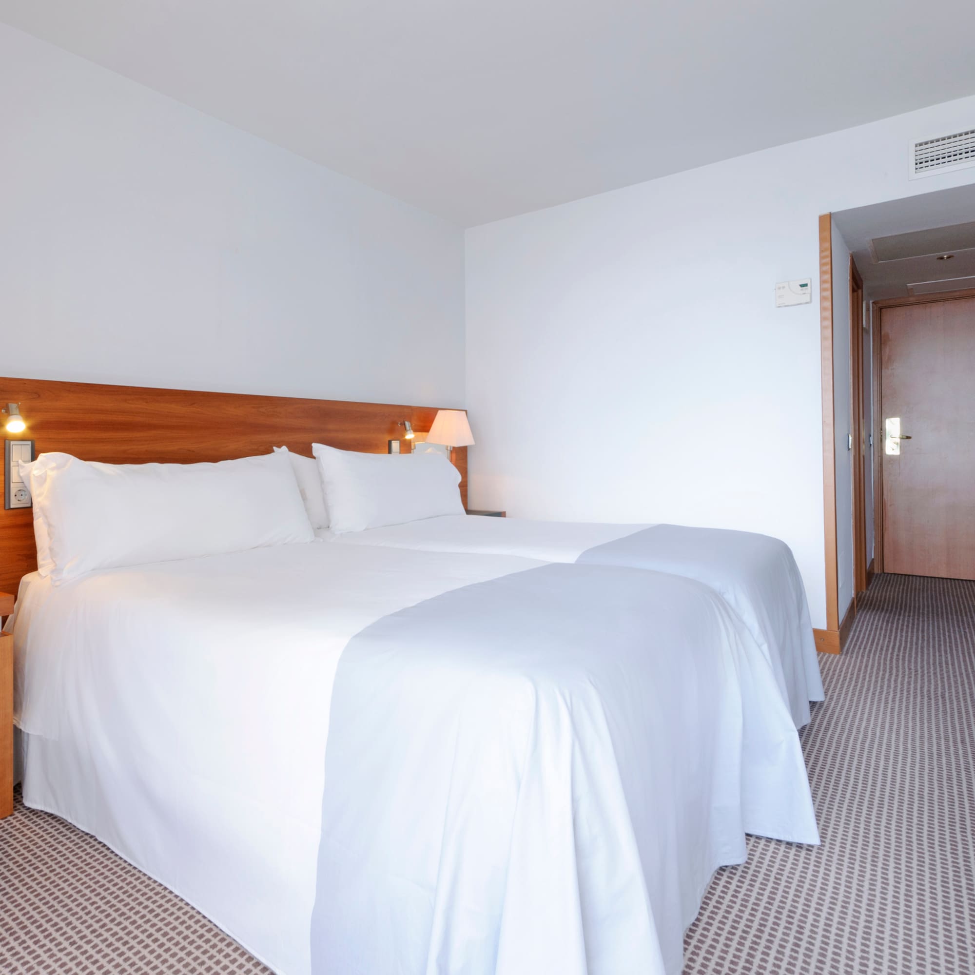 a bed with white sheets and a wood headboard in a hotel room