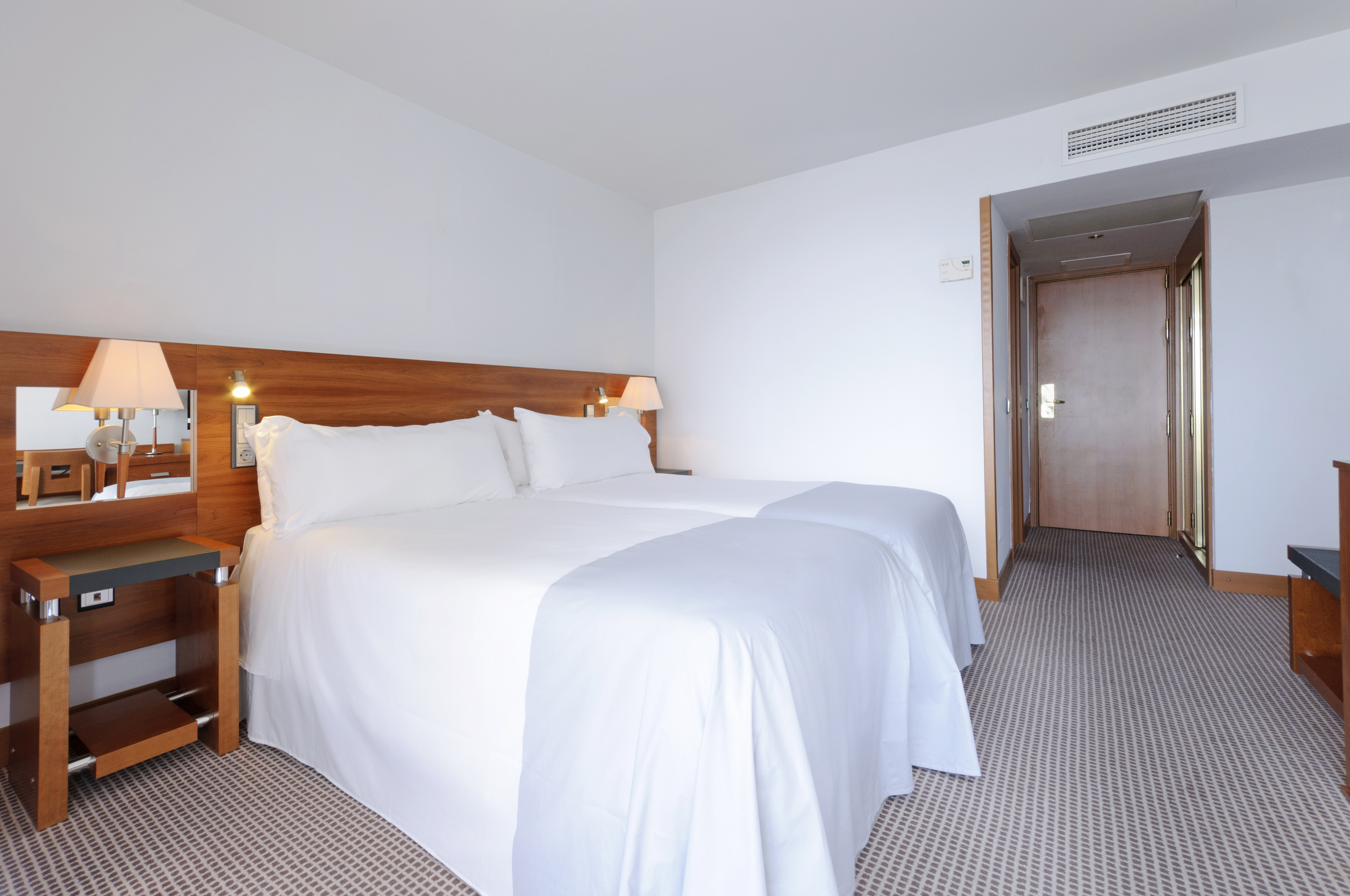 Modern hotel room with two single beds, white linens, and wooden accents.