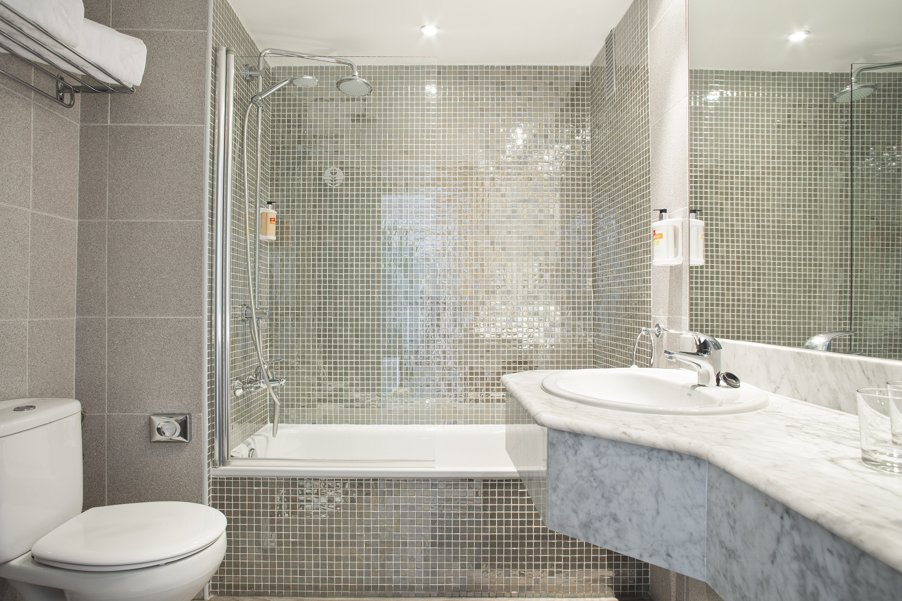 Modern hotel bathroom with tiled shower-bathtub, toilet, and marble vanity.