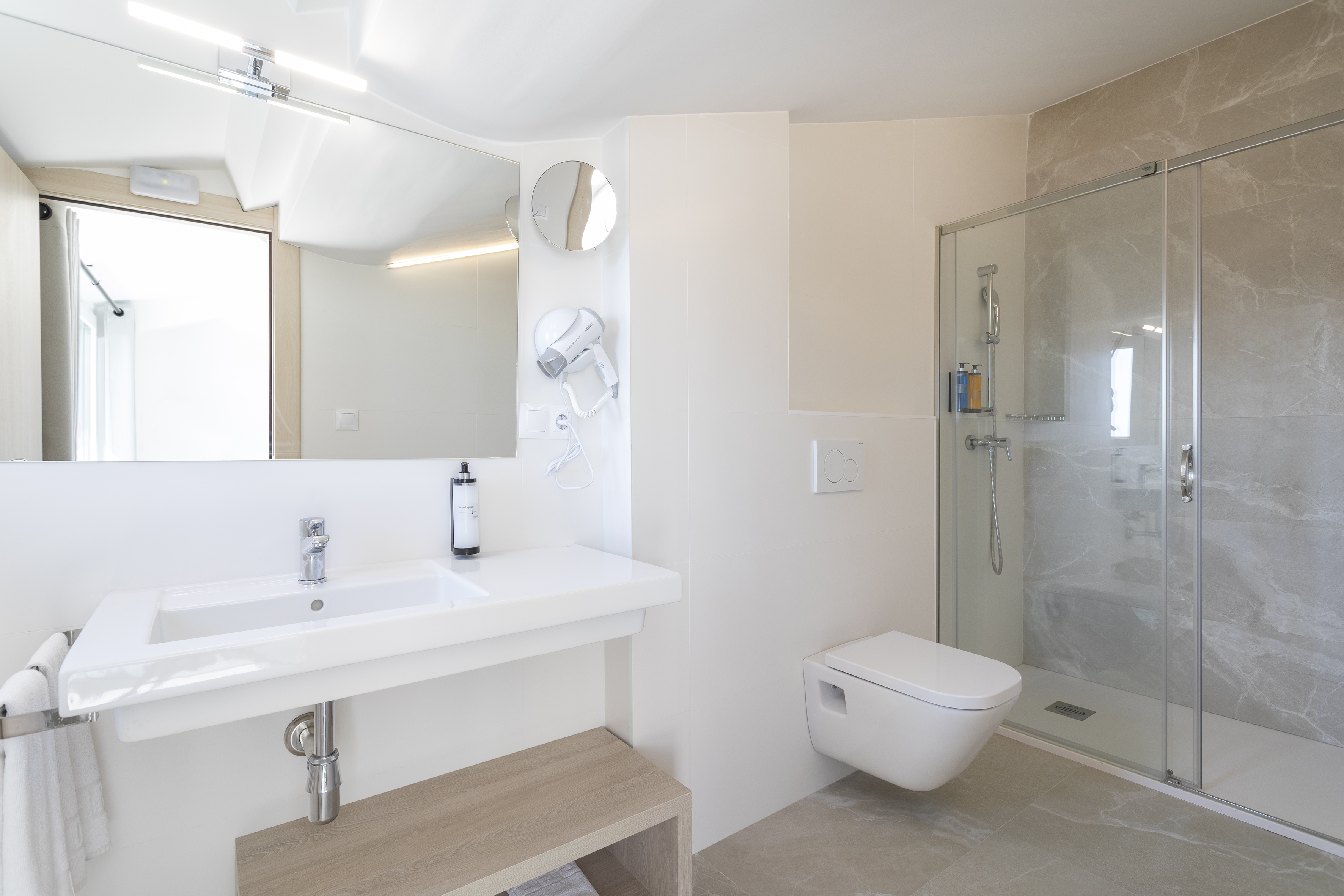 Modern white bathroom featuring a vanity, wall-mounted toilet, and glass shower.