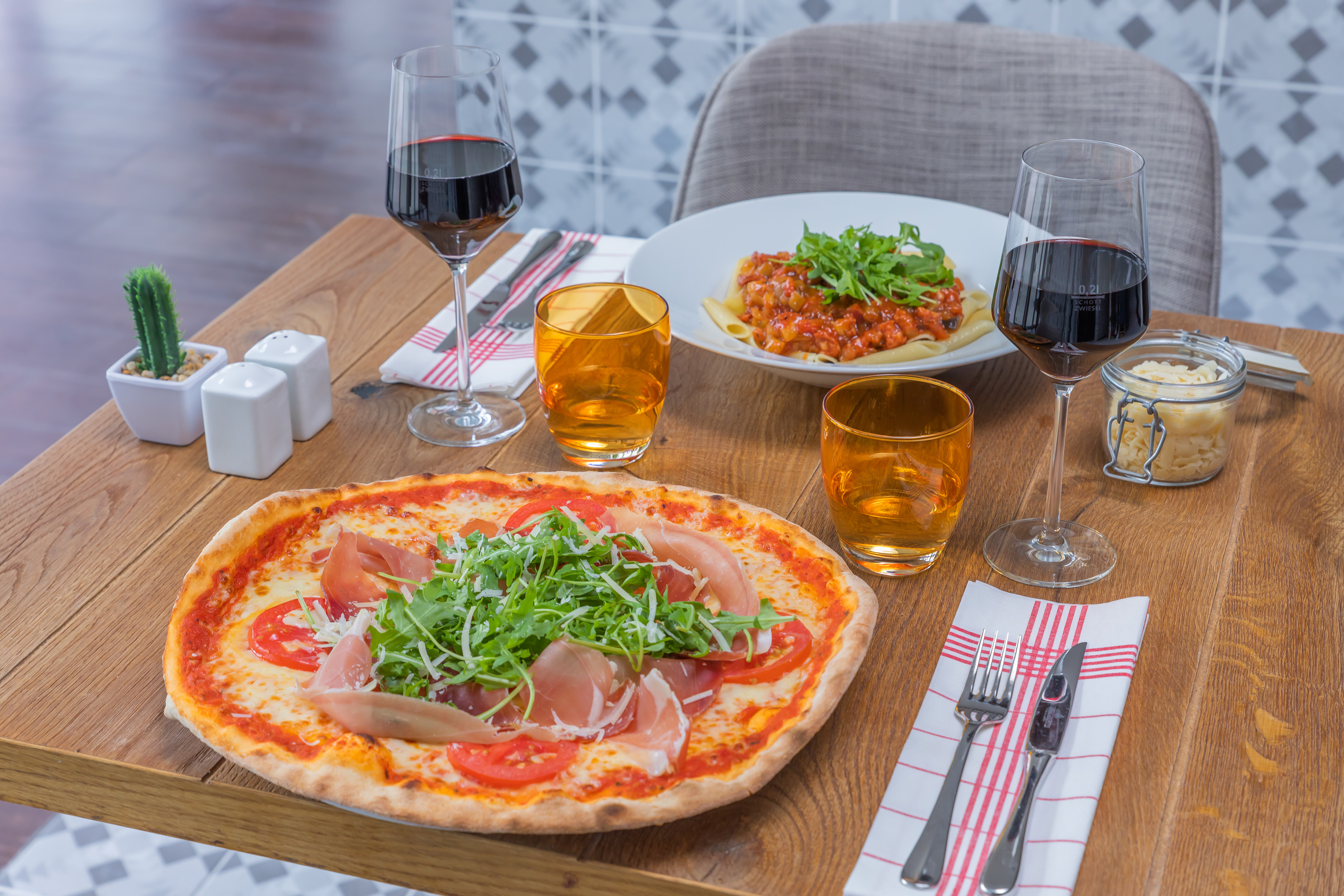 Pizza with prosciutto and arugula, pasta bolognese, red wine on wooden table.