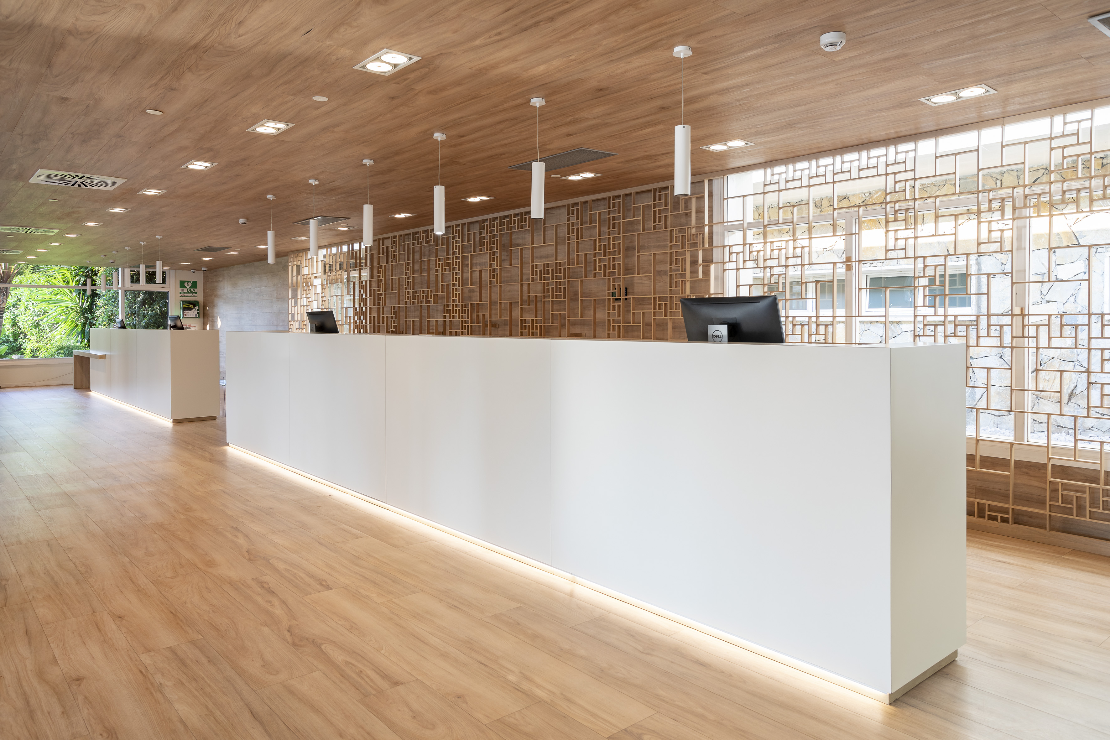 Modern hotel reception with white desks, wood ceiling, and decorative screen.