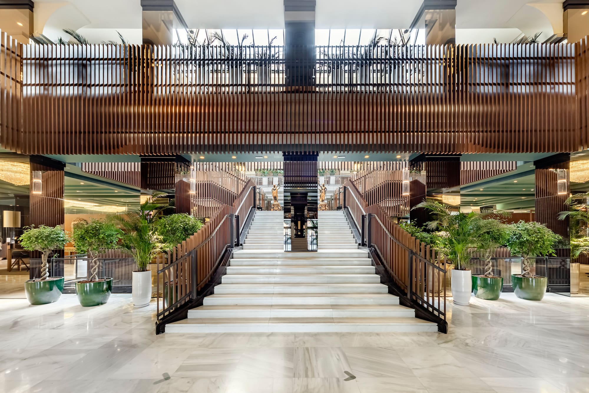 Modern luxury hotel lobby, grand marble staircase, wood slats, and plants.