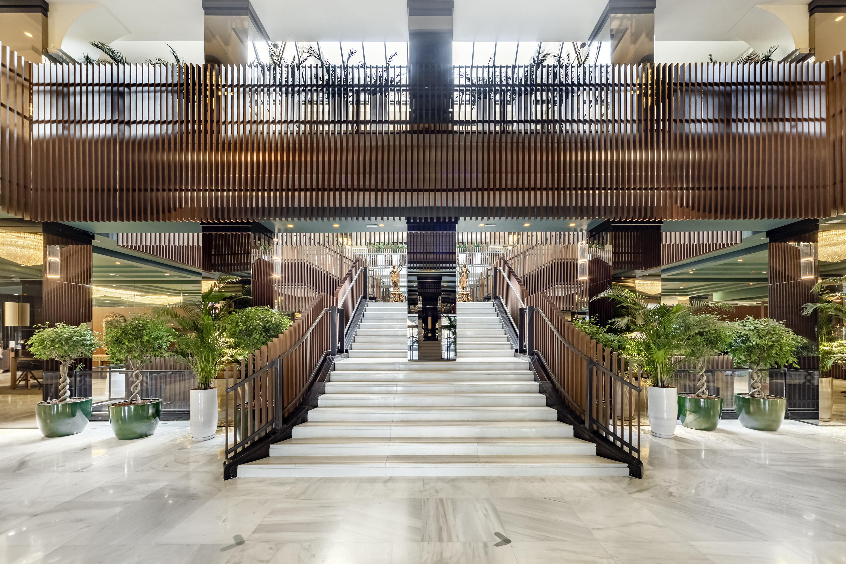 Modern luxury hotel lobby, grand marble staircase, wood slats, and plants.