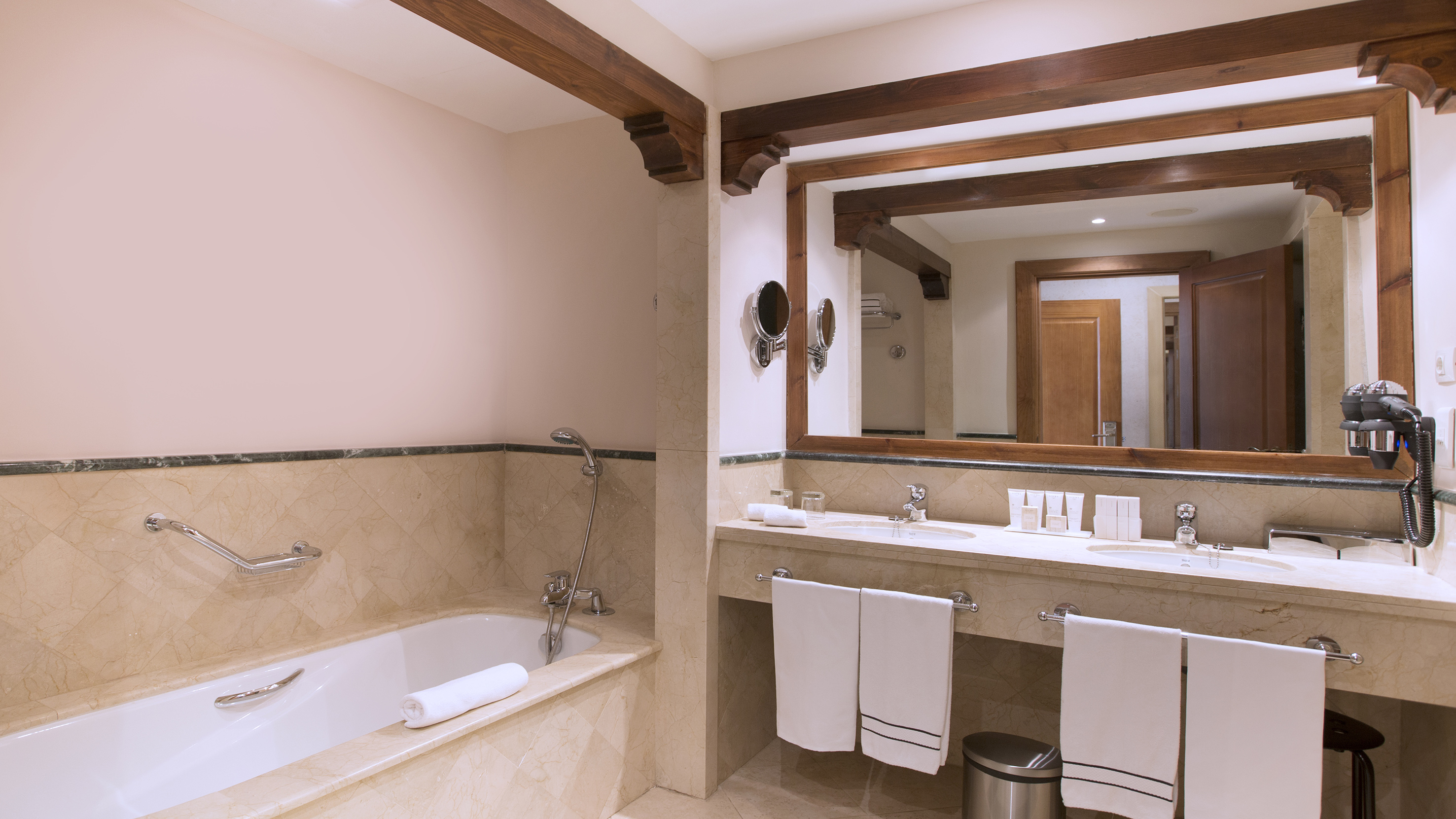 Luxury marble bathroom with double vanity, bathtub, large mirror, and wooden accents.