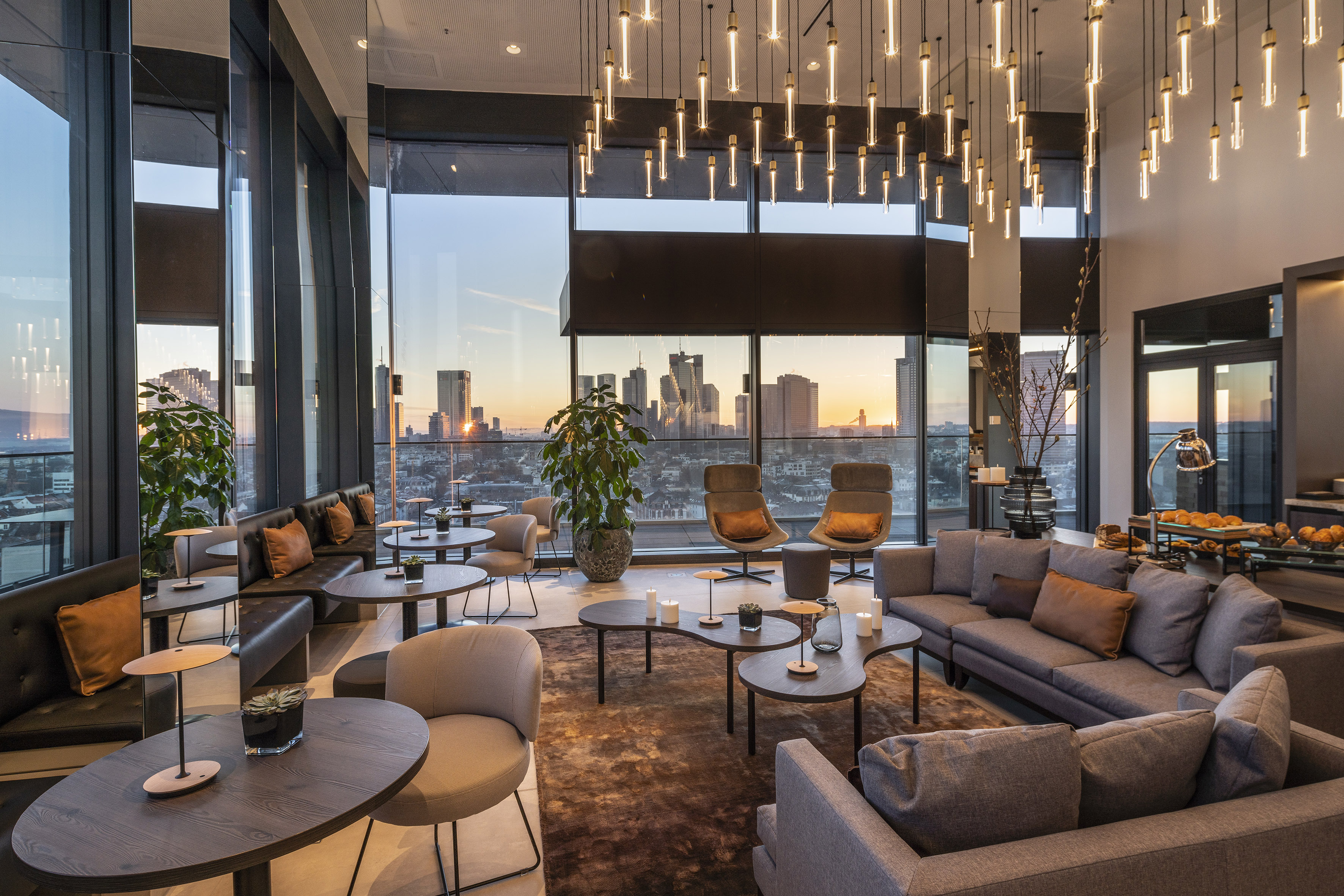 Modern lounge with city skyline sunset view, stylish seating, and pendant lights.