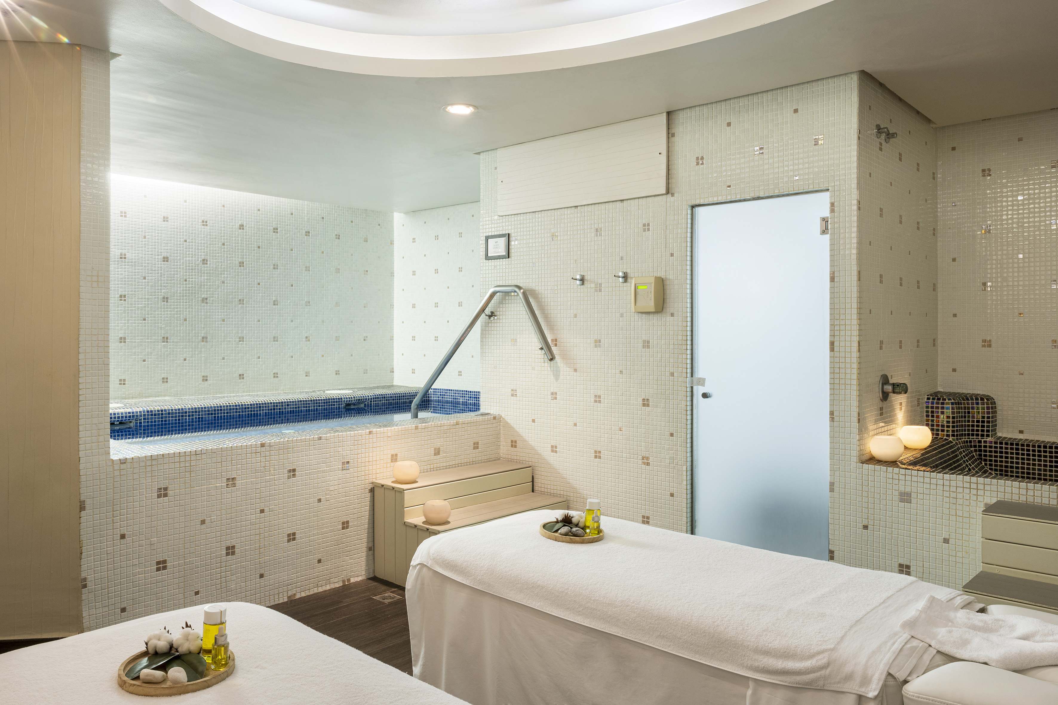 Spa massage room with jacuzzi, two therapy beds, and soothing mosaic tiles.