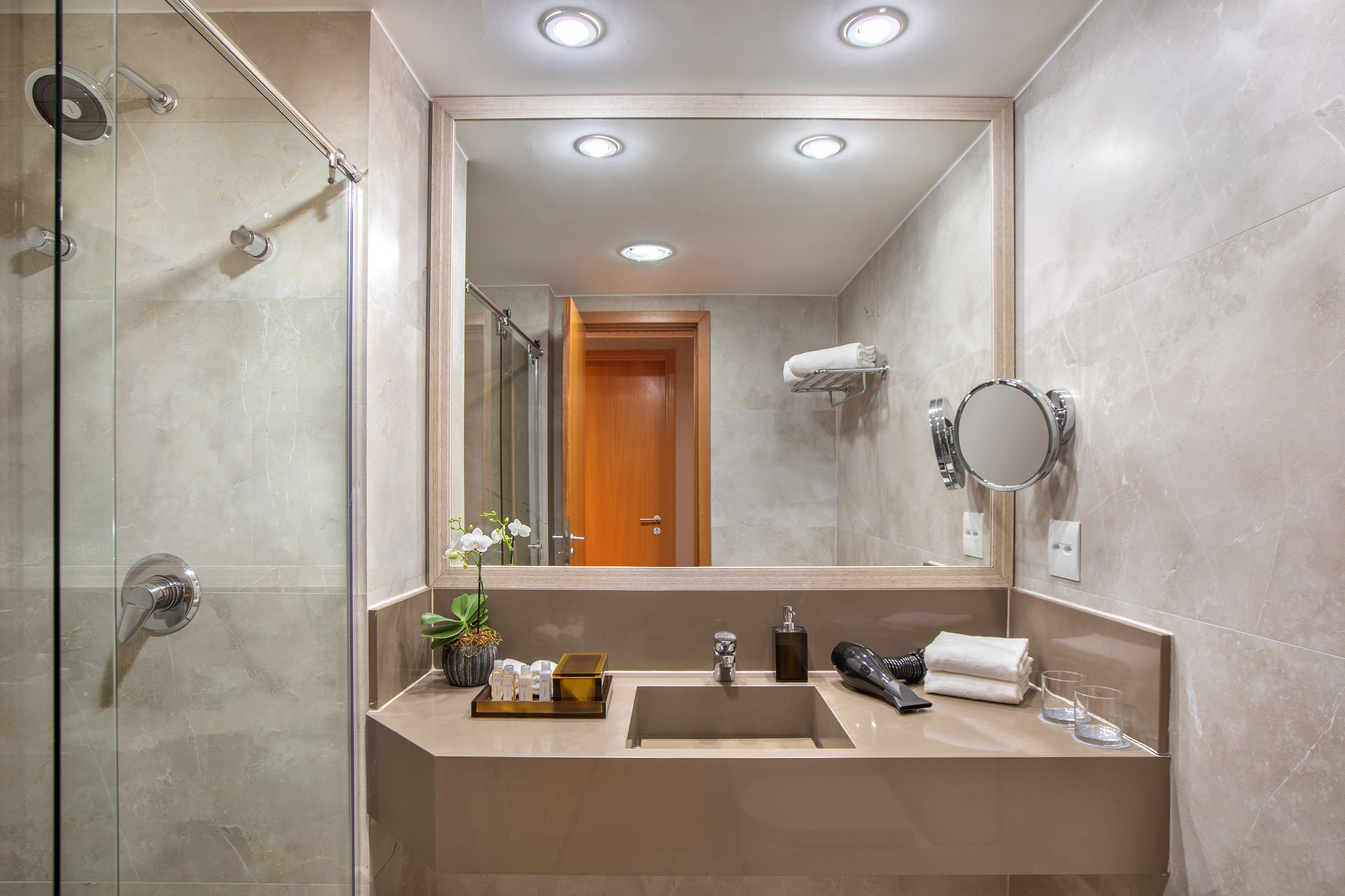 Modern marble hotel bathroom with vanity, large mirror, and glass shower.