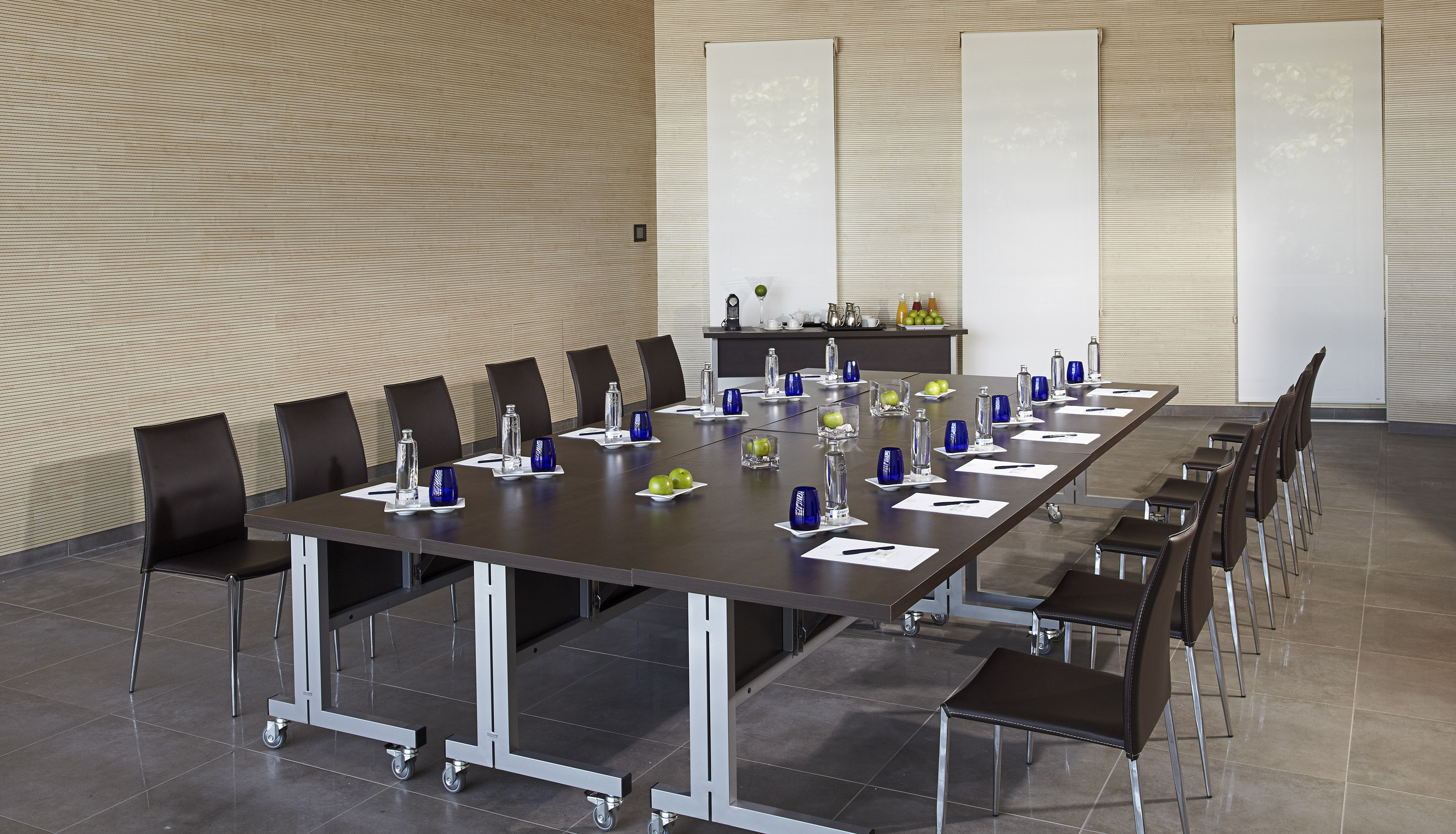 Modern conference room with long table, chairs, and refreshments setup.