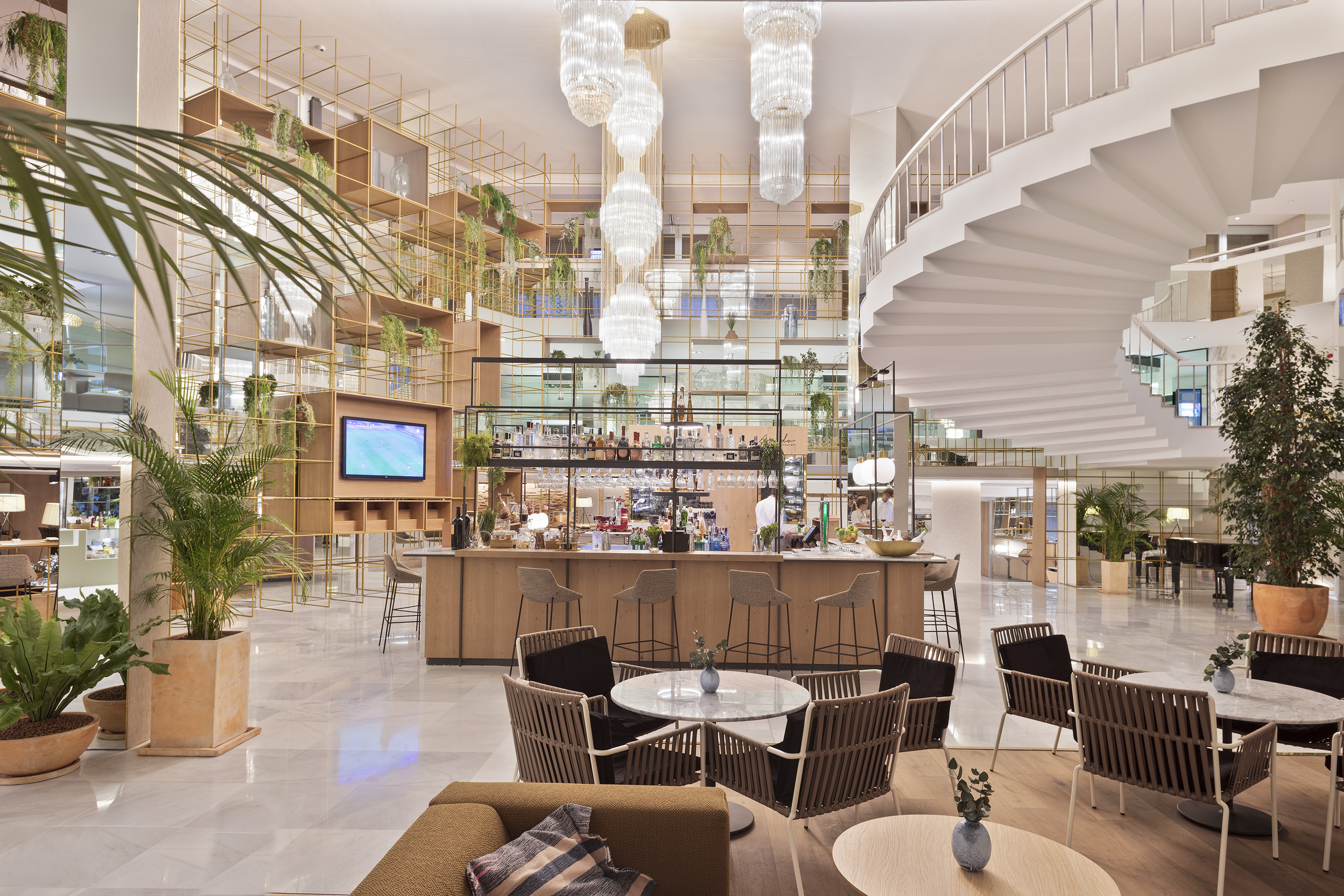 Hotel lobby bar, lounge, spiral staircase, and modern plant-filled interior.