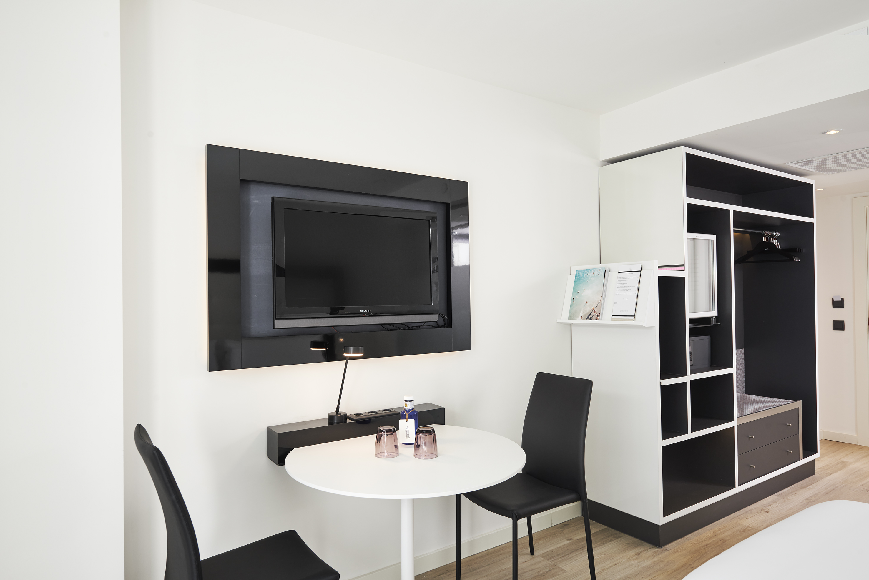 Modern hotel room with TV, round table, and open black and white wardrobe.