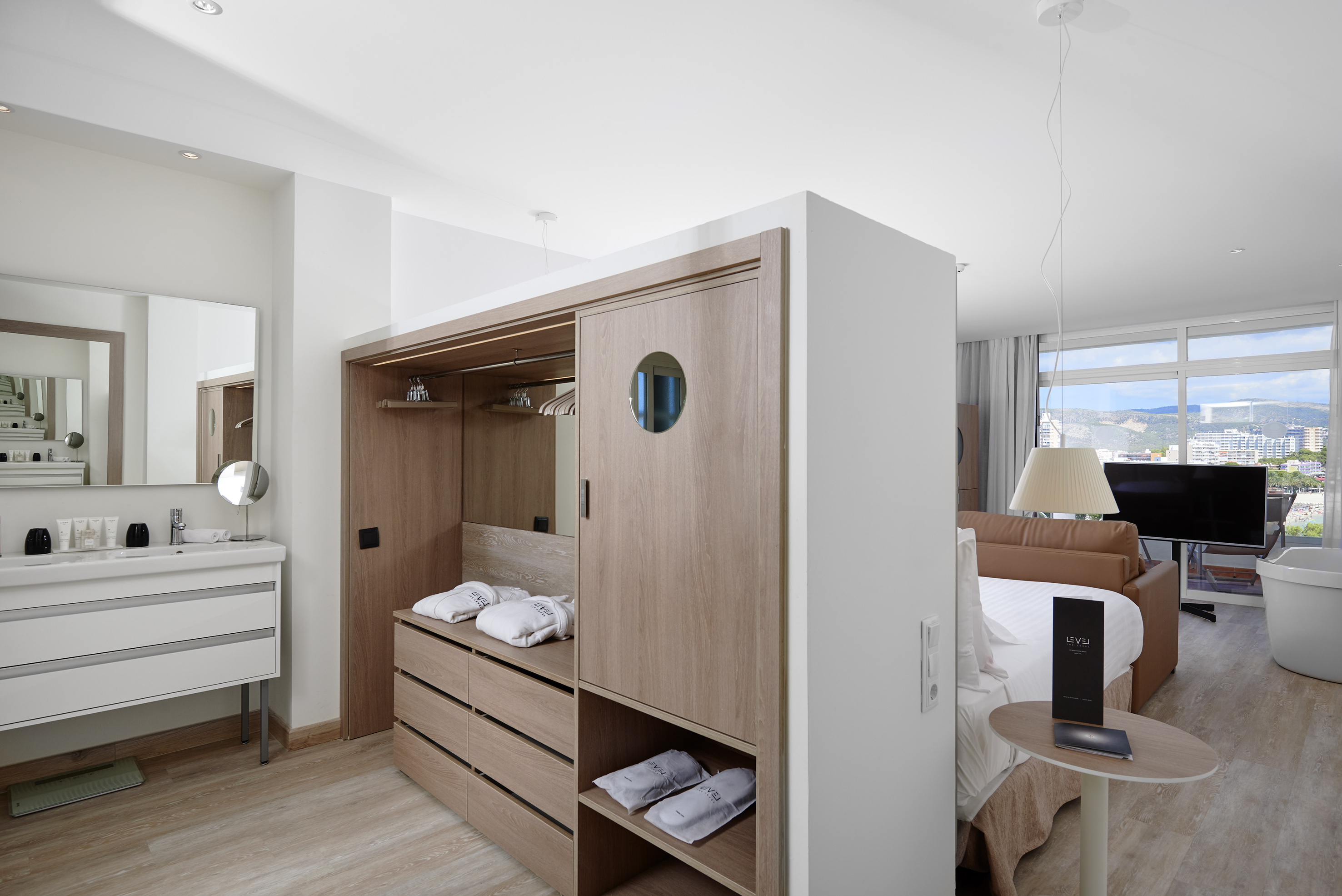 Modern hotel room with wood wardrobe, vanity area, and city skyline view.