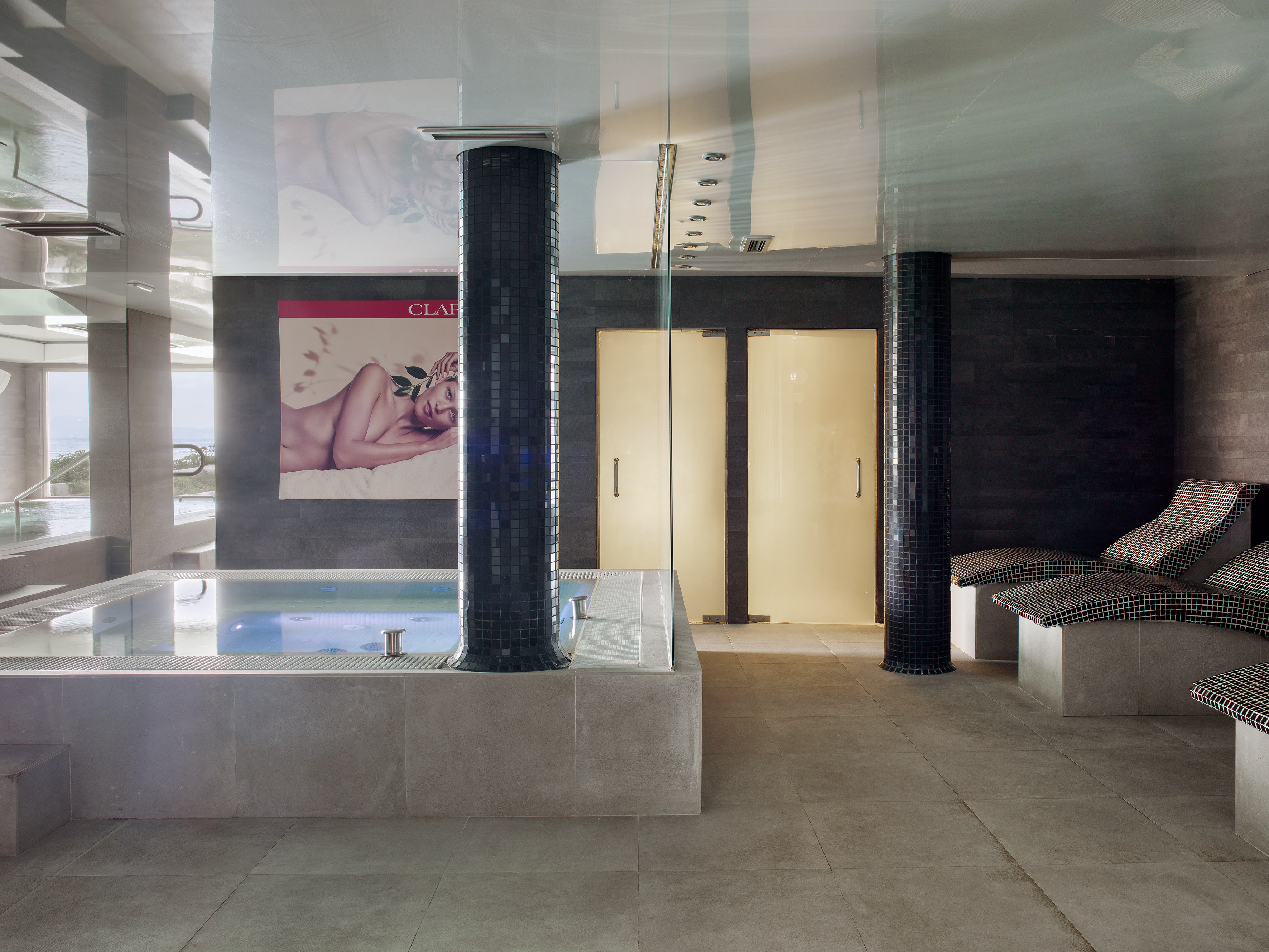 Spa interior with illuminated jacuzzi, tiled columns, and relaxation loungers.