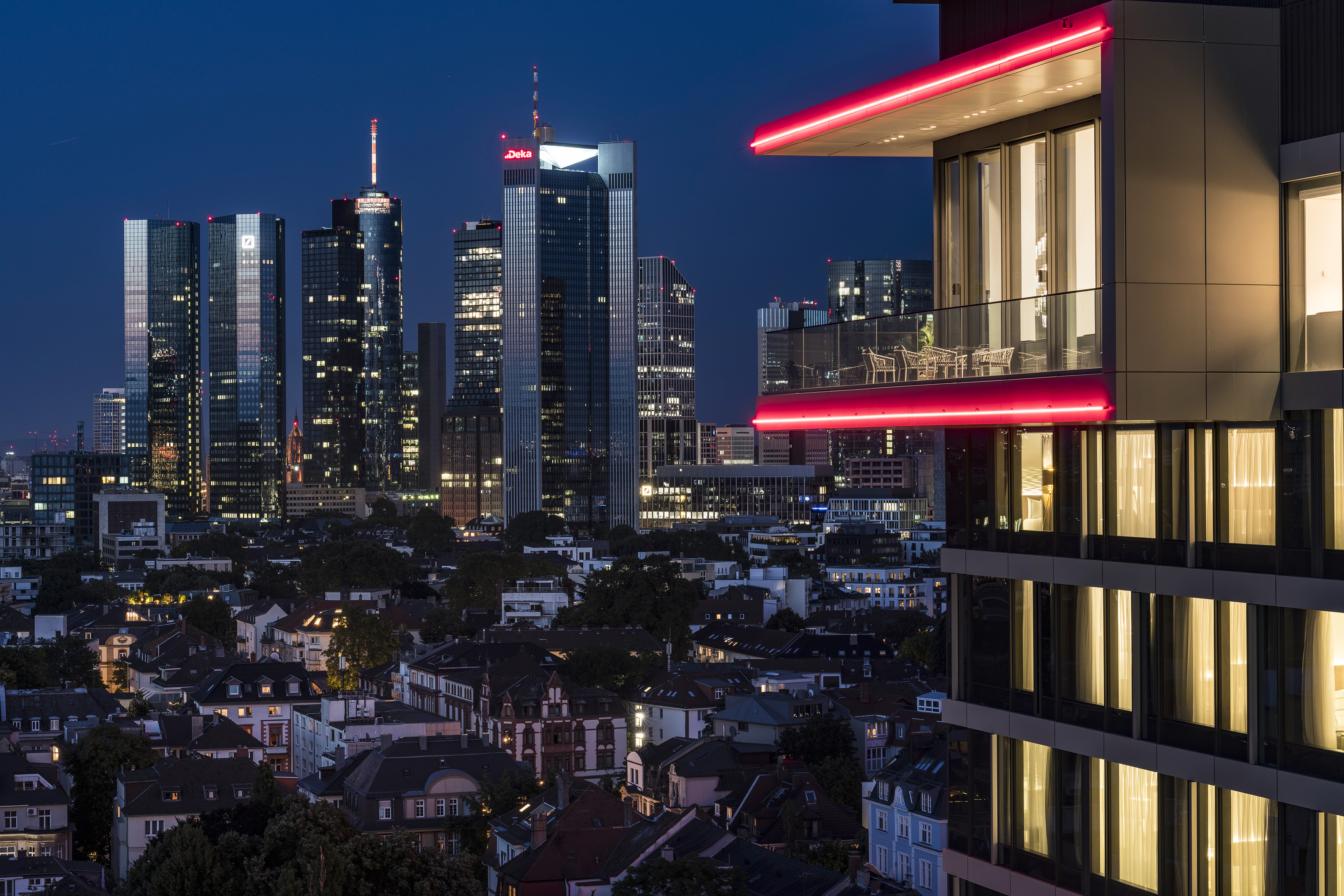 Frankfurt skyline at night, modern building with red neon, residential roofs below.