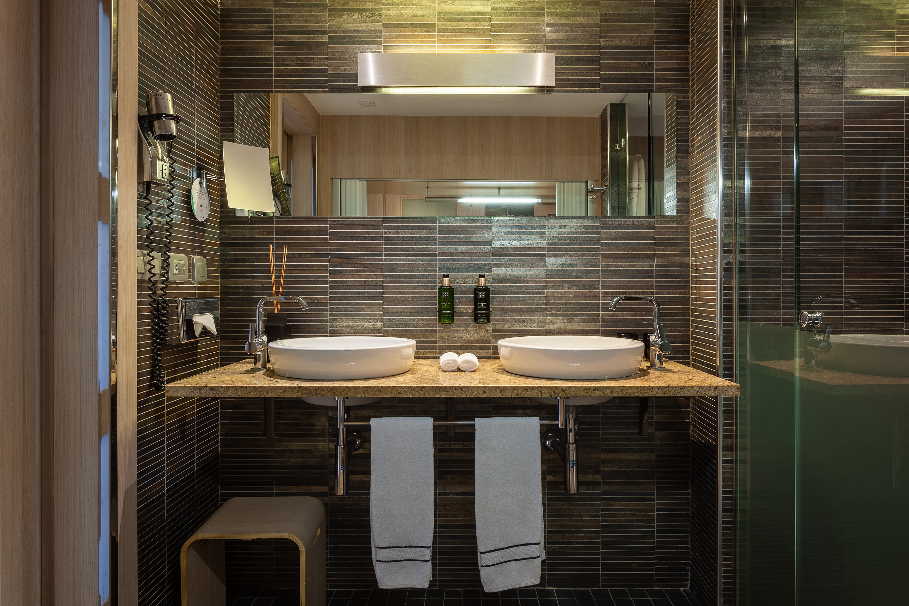 Modern bathroom with dual sinks, dark tile, marble counter, and glass shower.