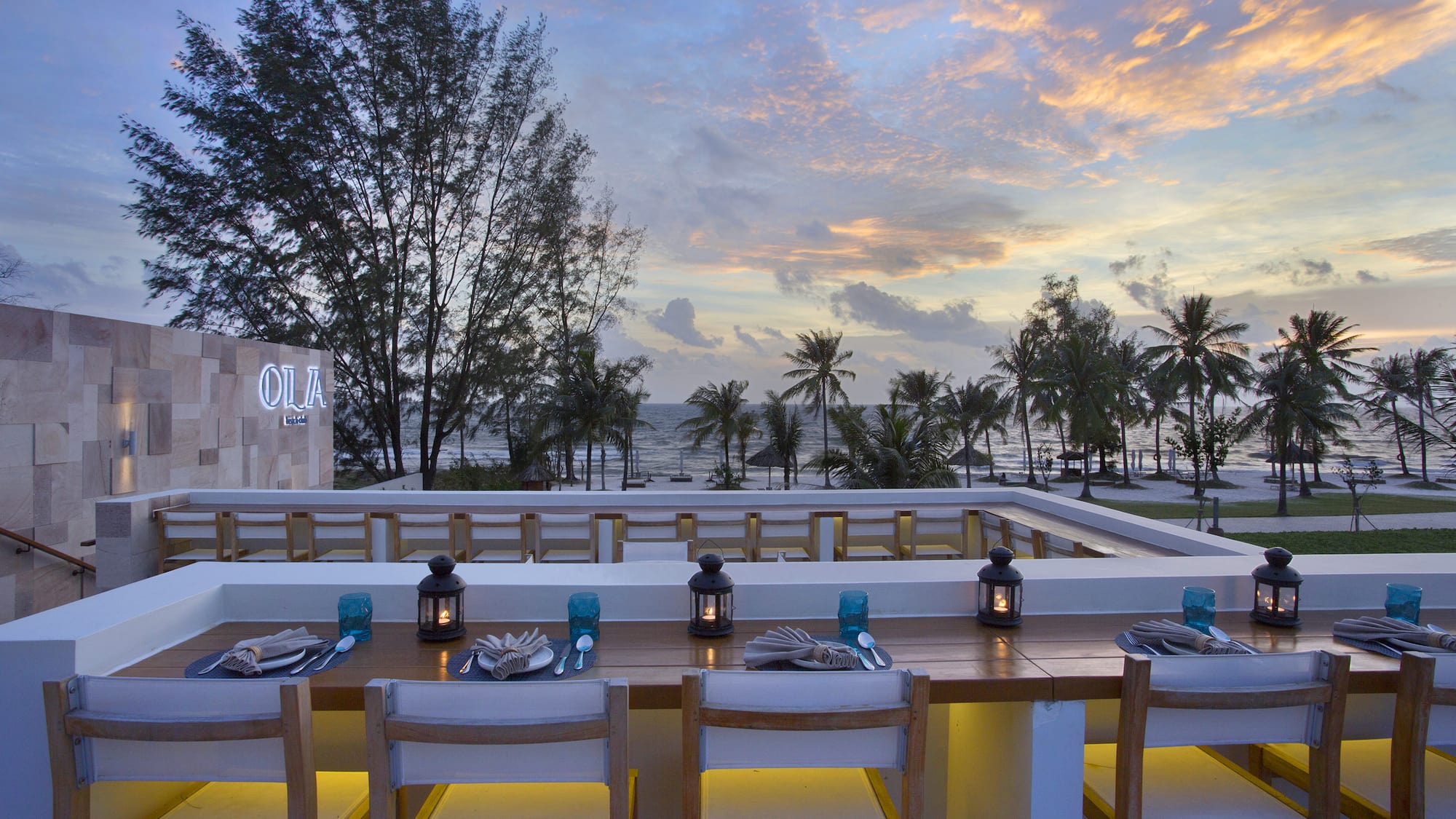 a table set for dinner with a view of the ocean and trees