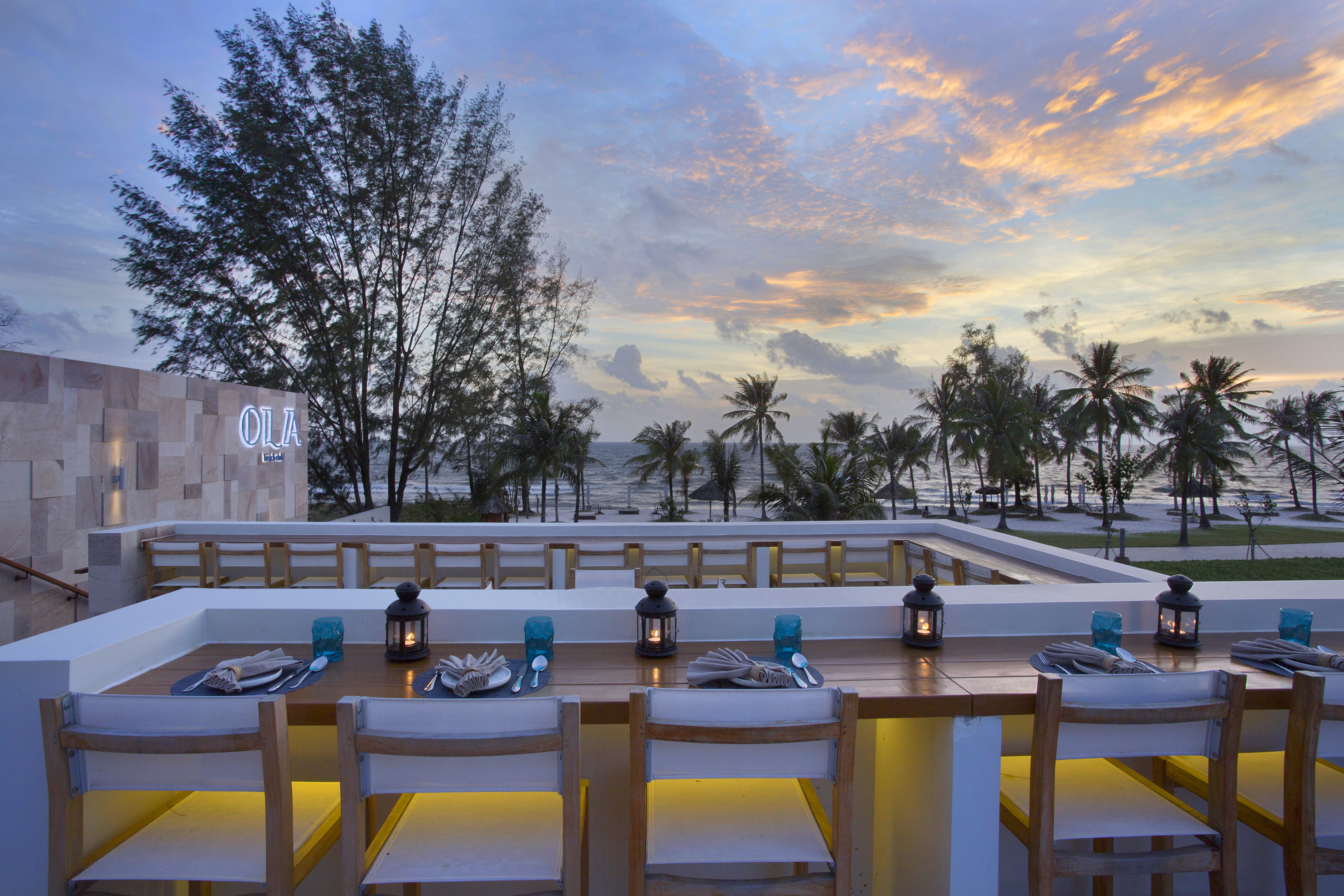 a table set for dinner with a view of the ocean and trees