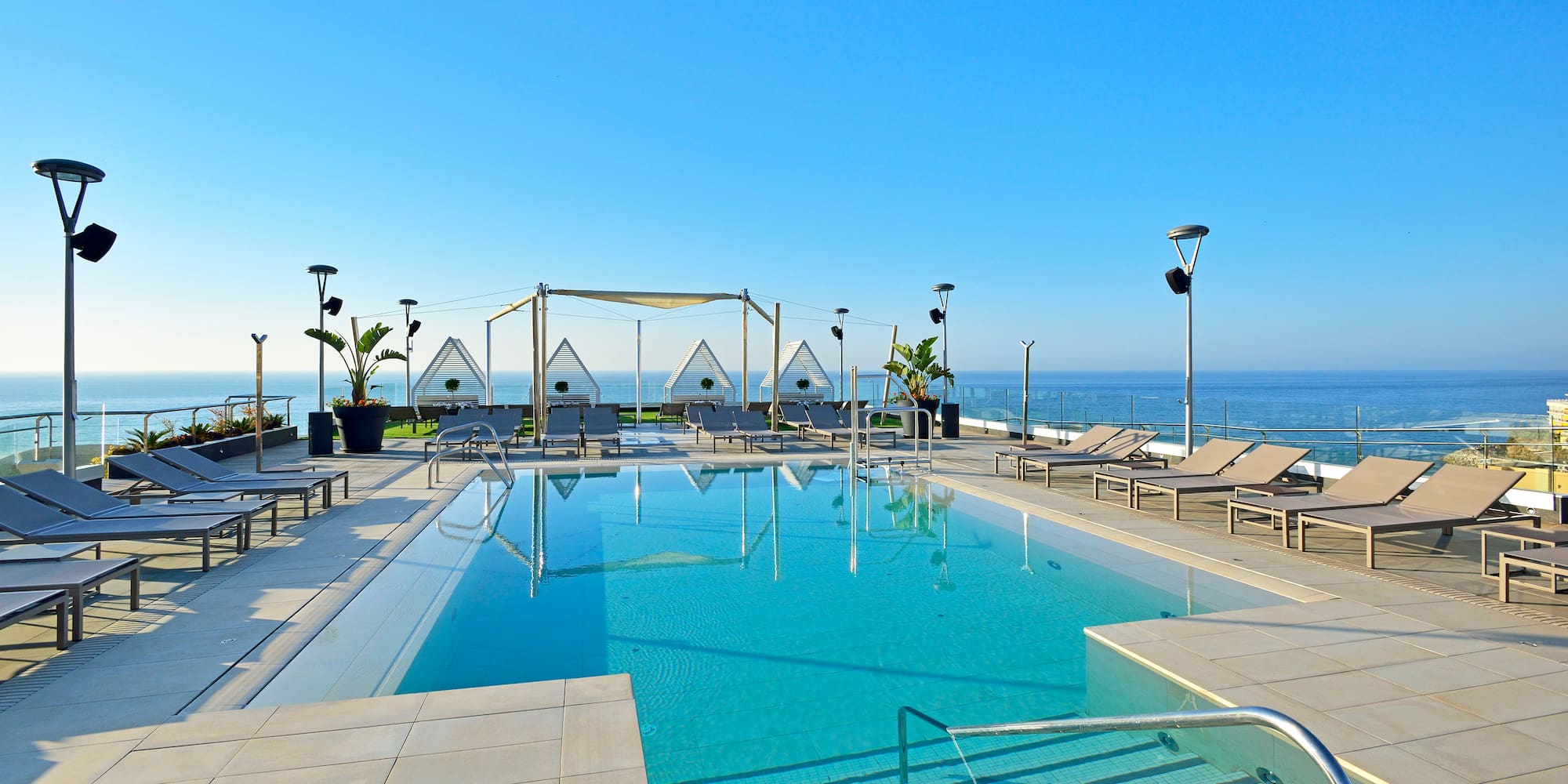 a pool with chairs and a deck chair on a rooftop overlooking the ocean