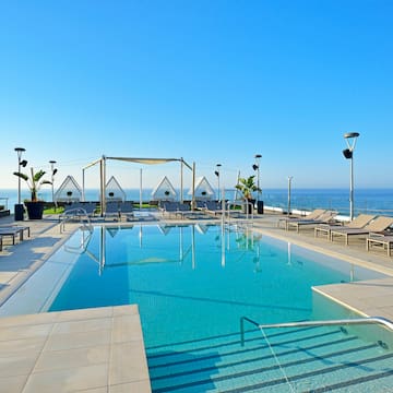 a pool with chairs and a deck chair on a rooftop overlooking the ocean